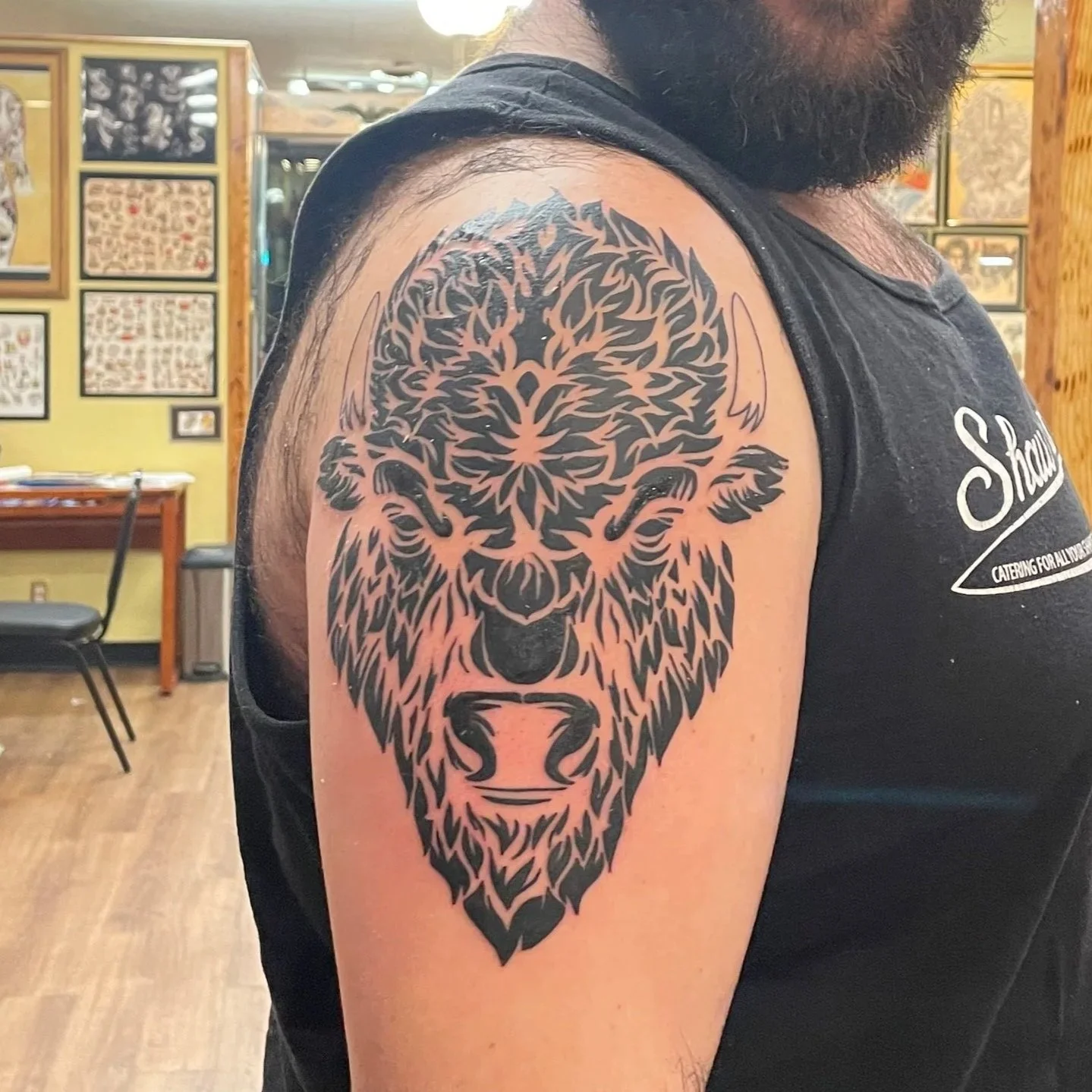 Tattoo of a bison's face on a person's upper arm, featuring a black tribal style design.