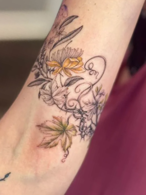 A tattoo of flowers and leaves with a mix of colored and black ink on a person's arm.
