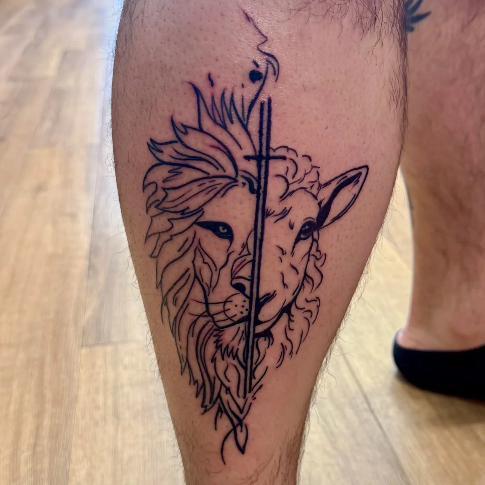 Tattoo of a lion's face with a spear going through its head, located on a person's leg.
