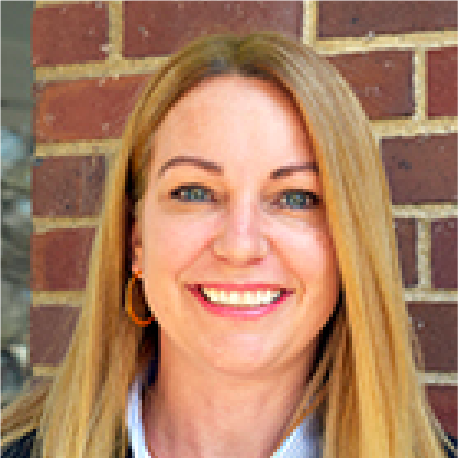 A woman with long blonde hair smiling in front of a brick wall.