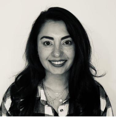 A smiling woman with long dark hair, wearing a plaid shirt and layered necklaces.