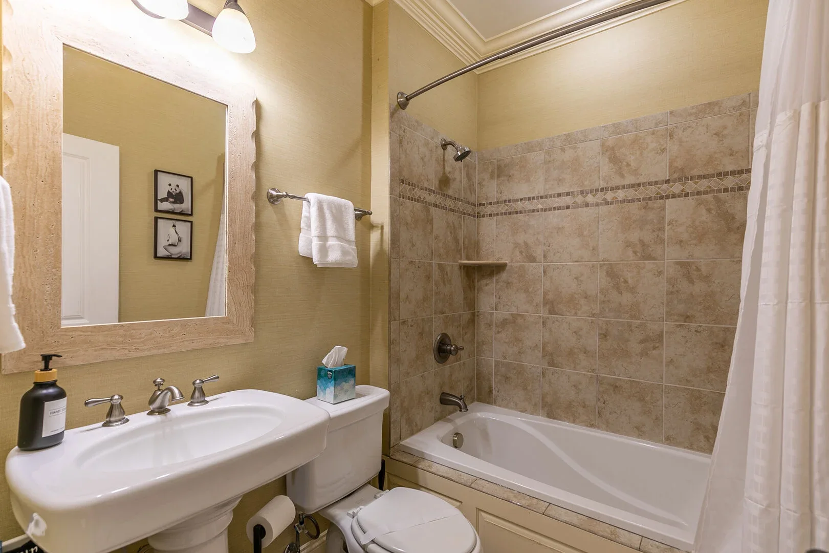Bathroom with a sink, mirror, toilet, and bathtub with shower curtain, beige tile walls, and a towel rack.