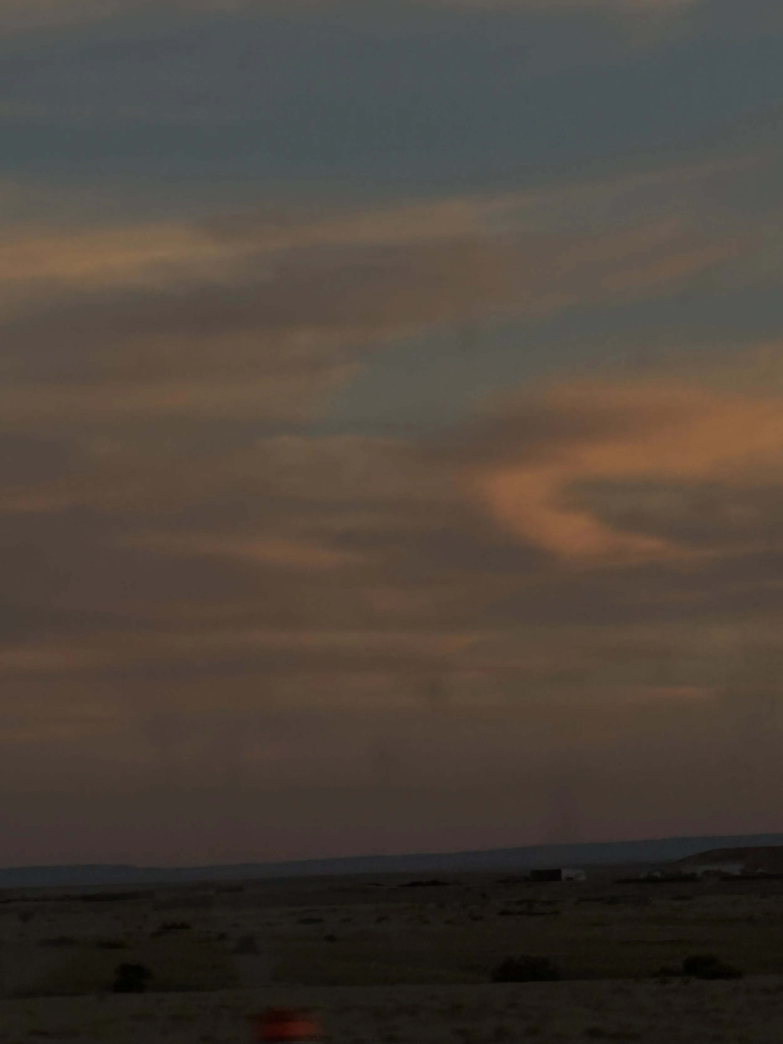 A landscape scene at sunset with a cloudy sky and a horizon in the distance.