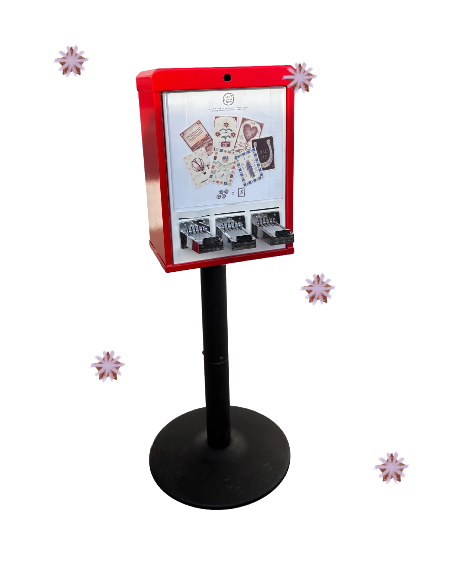 A red test card vending machine with small art prints displayed in the upper part and three coin slots with trays below.