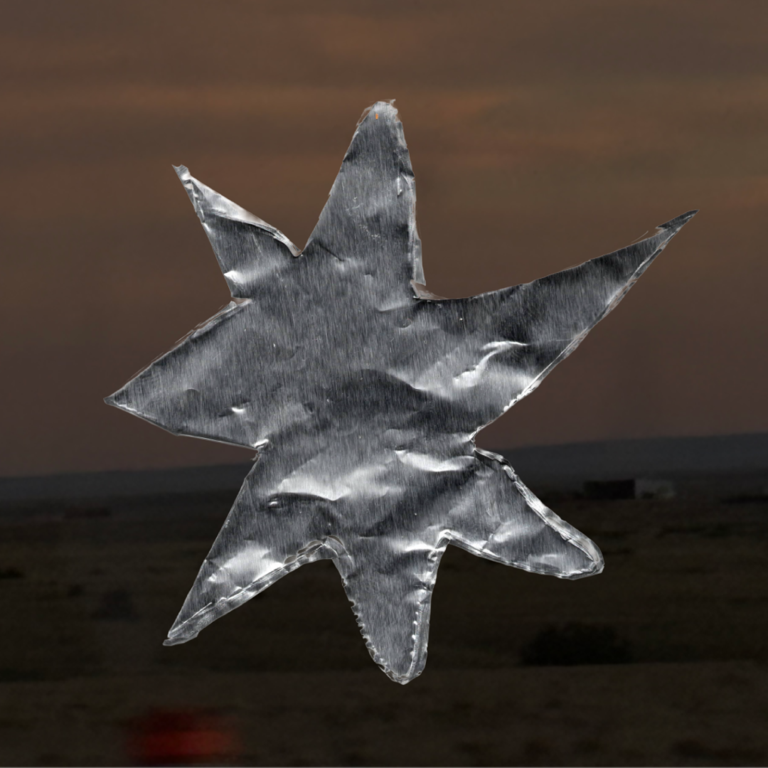 A star-shaped ornament made of crinkled aluminum foil against a dark and cloudy sky backdrop.