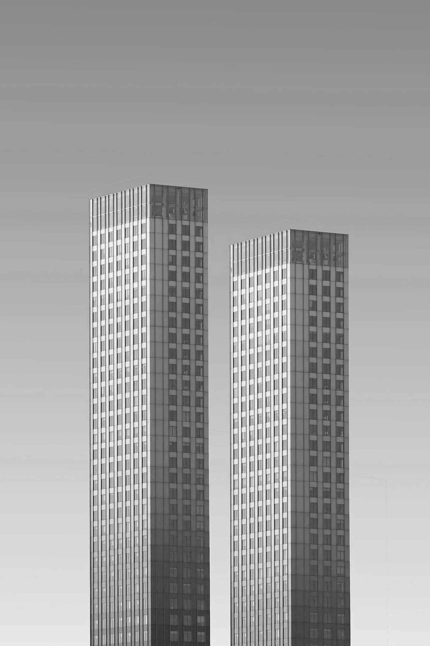 Two tall, identical office buildings with glass facades standing side by side against a clear sky.