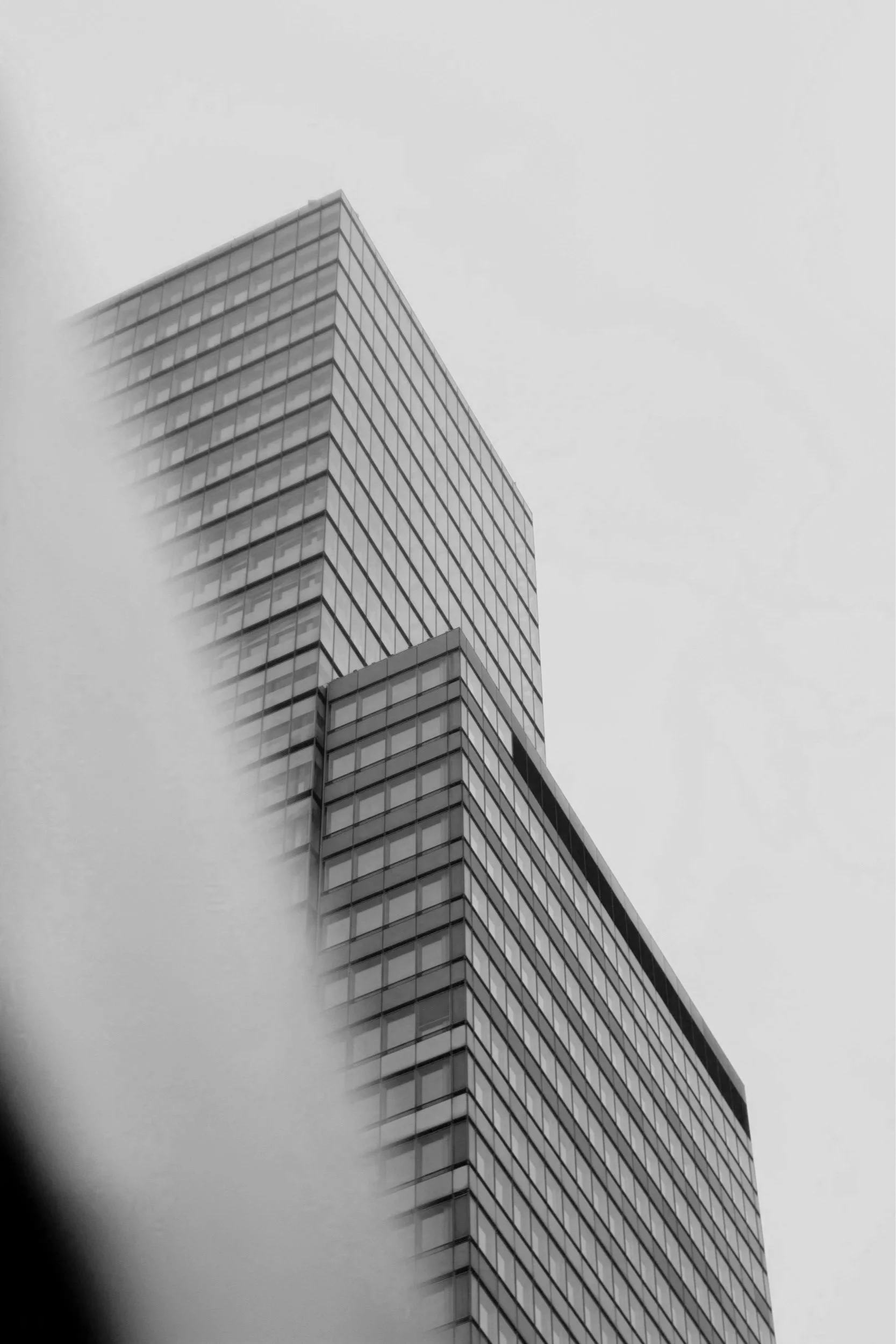 A tall modern building with glass windows, viewed from below against a cloudy sky.
