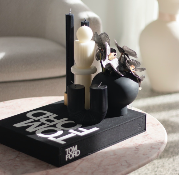 Decorative black and cream candles on a layered tray with leafy branches, placed on a pink marble side table.