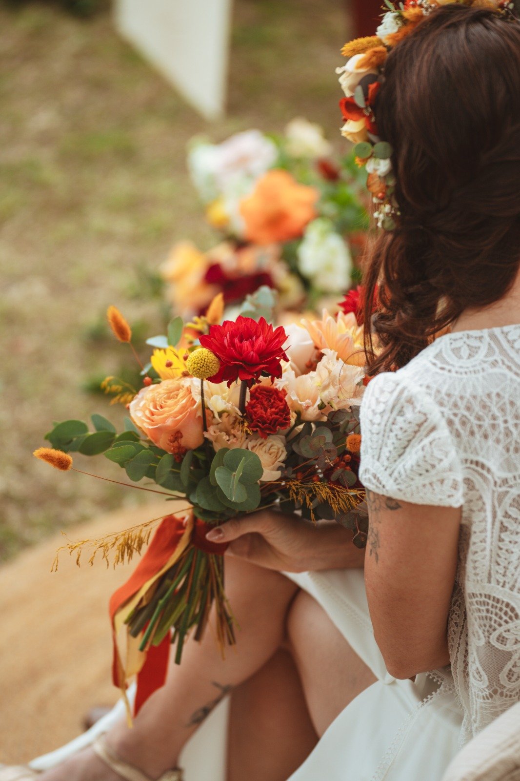 Femme tenant un bouquet de fleurs colorées lors d'une cérémonie, portant une robe en dentelle blanche.