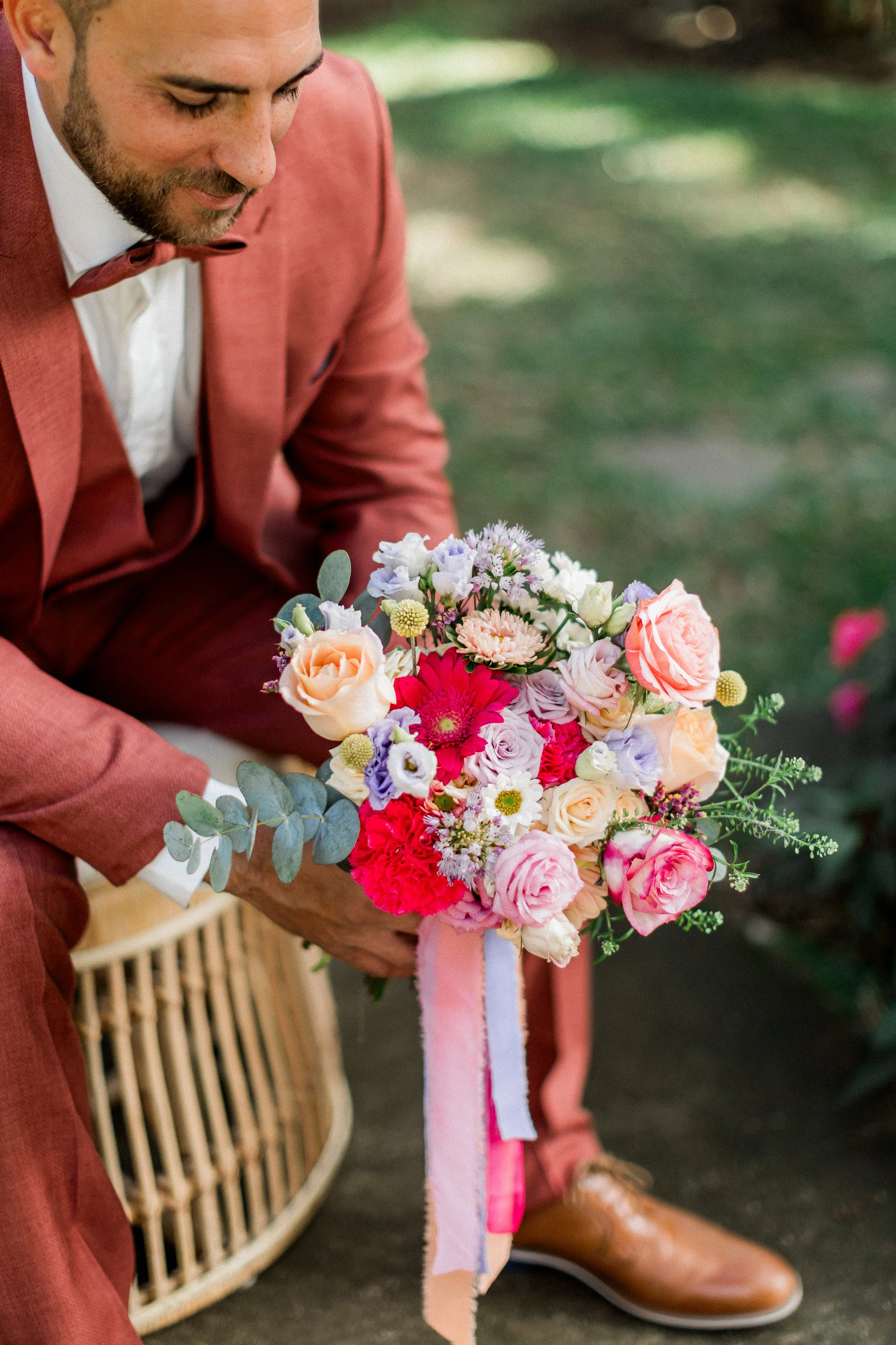 Un homme en costume rouge, tenant un bouquet de fleurs colorées dans un cadre extérieur.