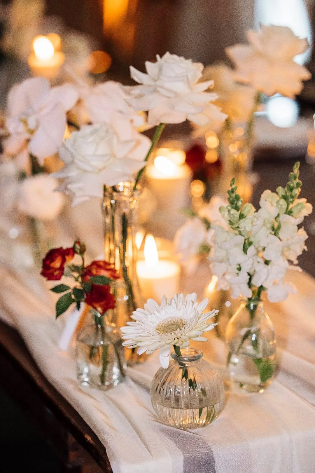 Vases contenant des fleurs blanches et rouges, décorations avec des bougies allumées sur une table.