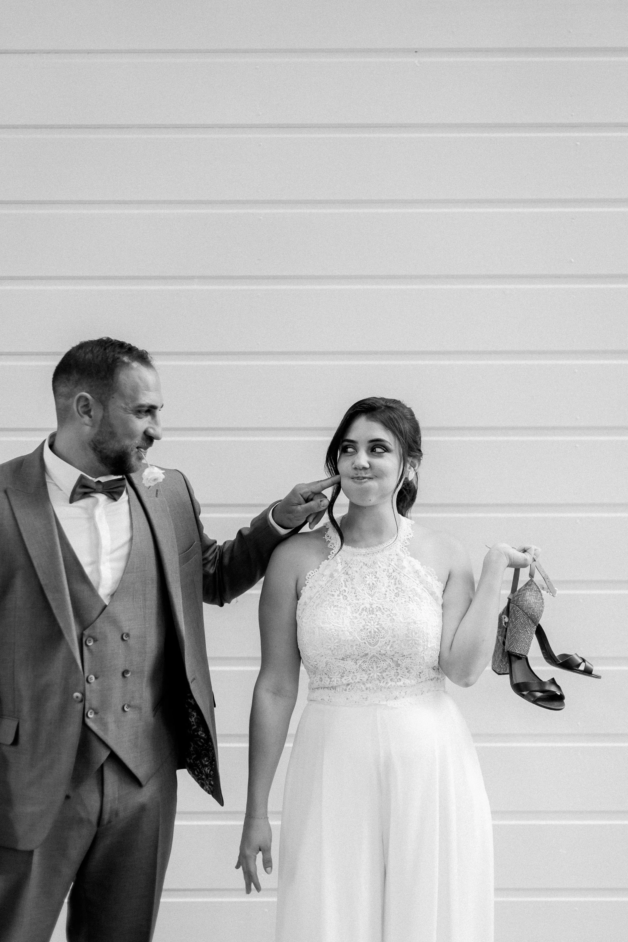 Un homme en costume tend une chaussure à une femme en robe de mariée, lors d'une séance photo de mariage.