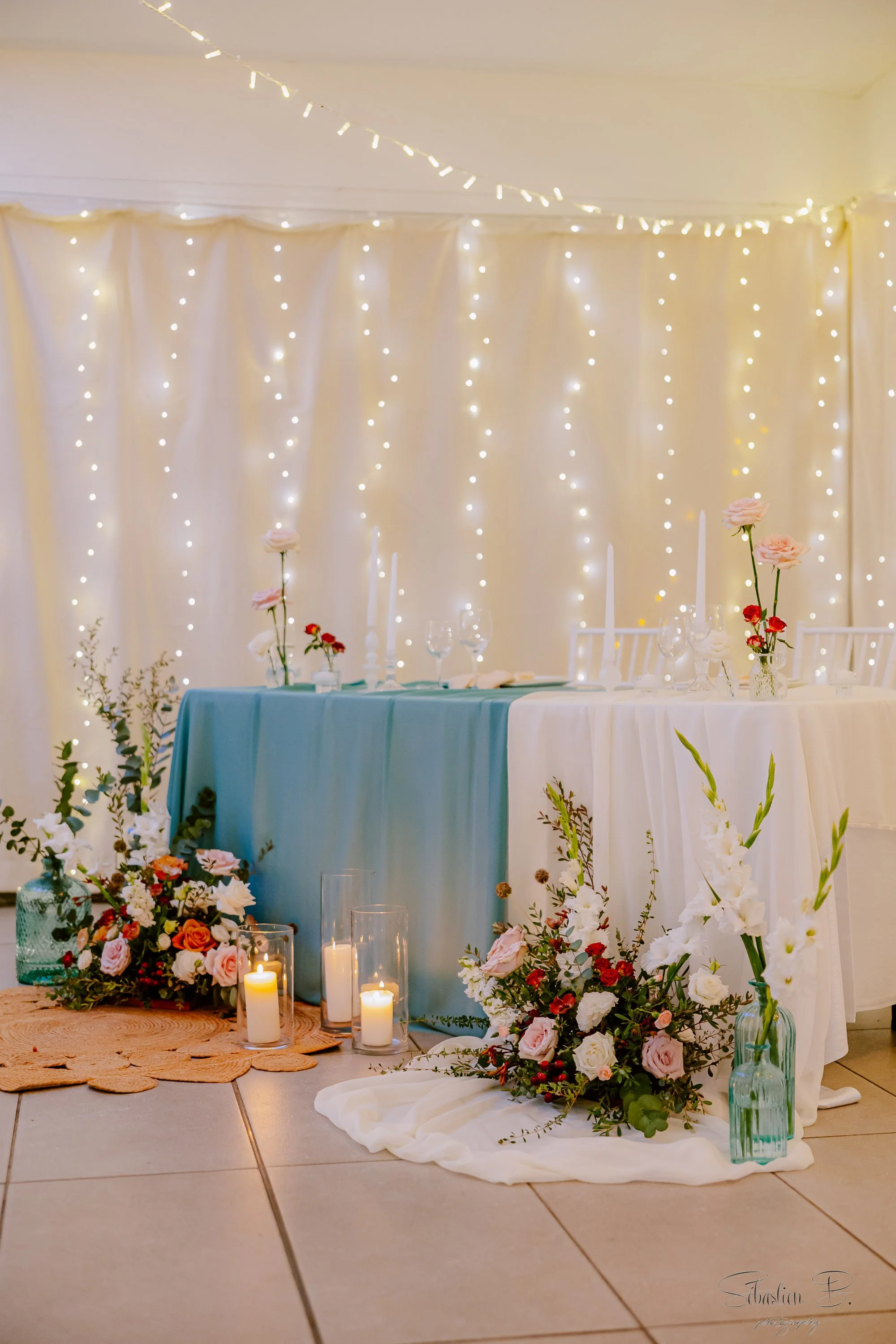 Décoration florale pour mariage avec des fleurs colorées, bougies et un fond de guirlandes lumineuses