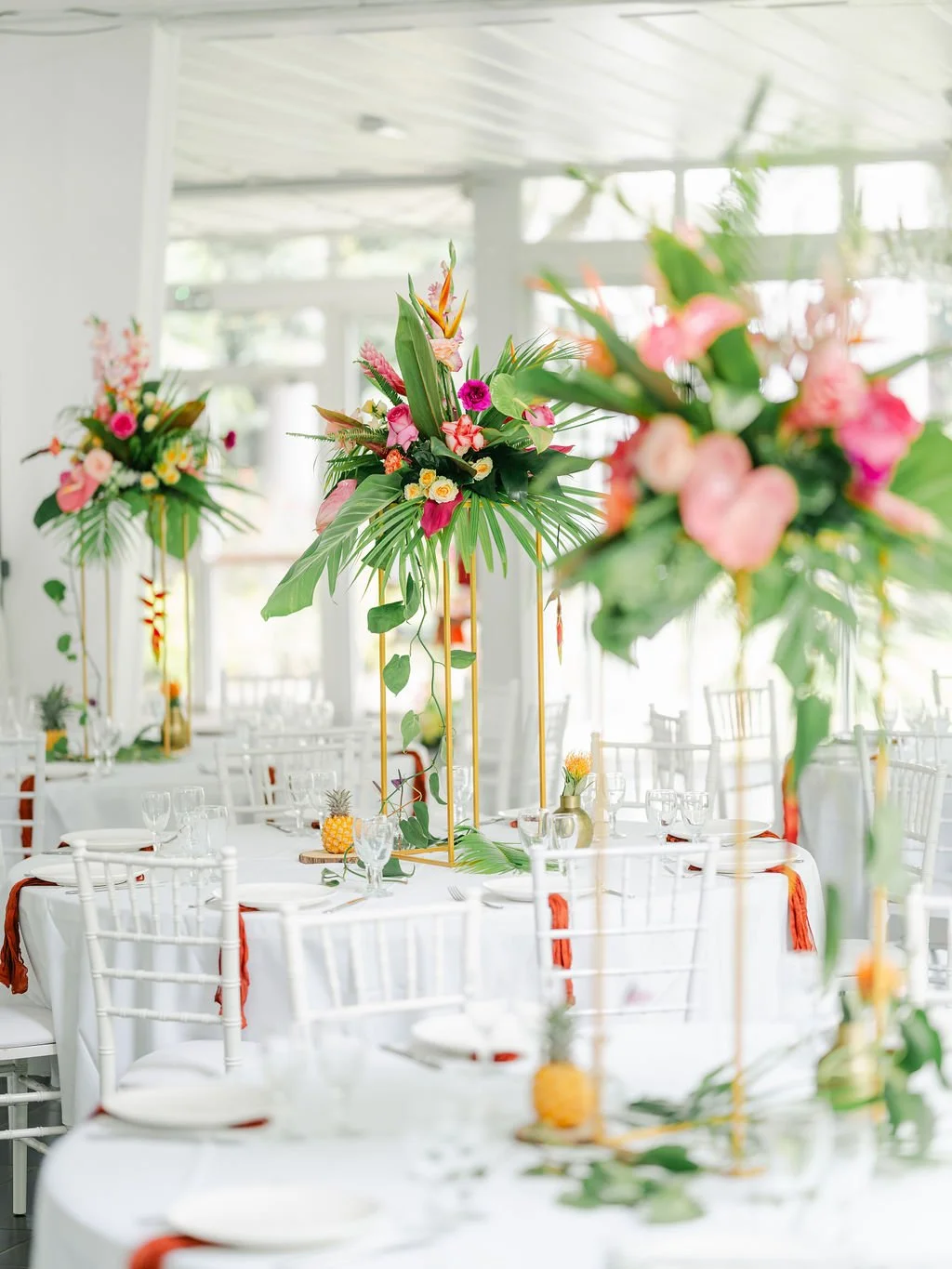 Décor de table pour un événement avec de grandes compositions florales tropicales sur un fond lumineux.