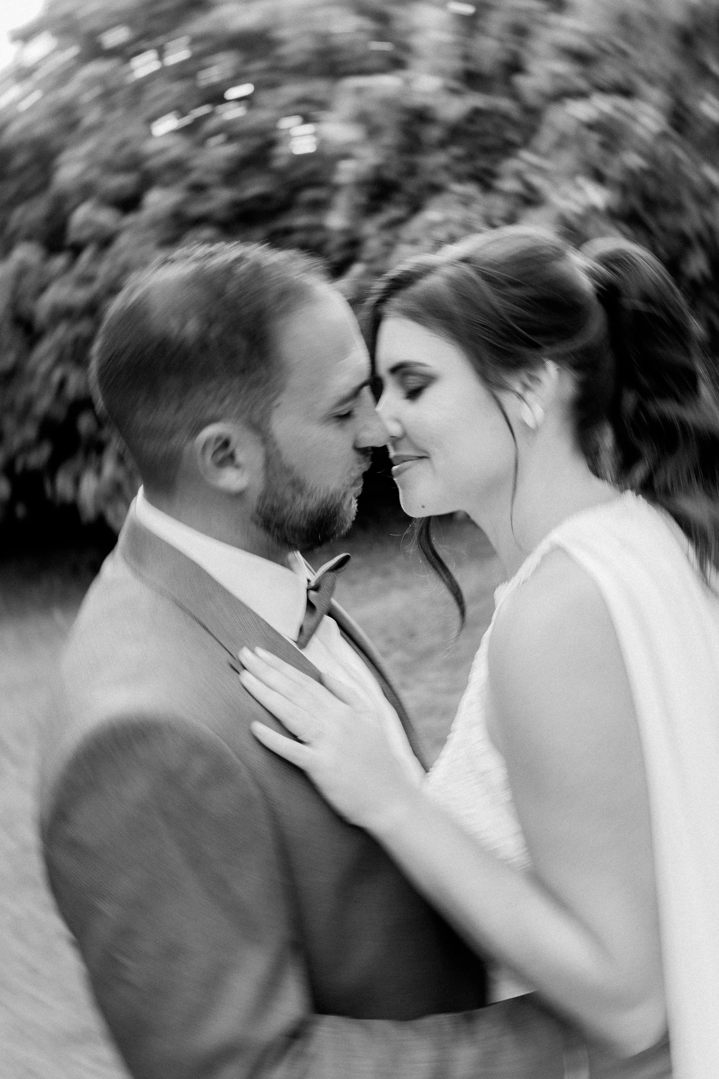 Un couple en robe de mariée et costume se regarde avec tendresse, la femme a les yeux fermés et le homme la regarde avec un sourire, dans un environnement naturel