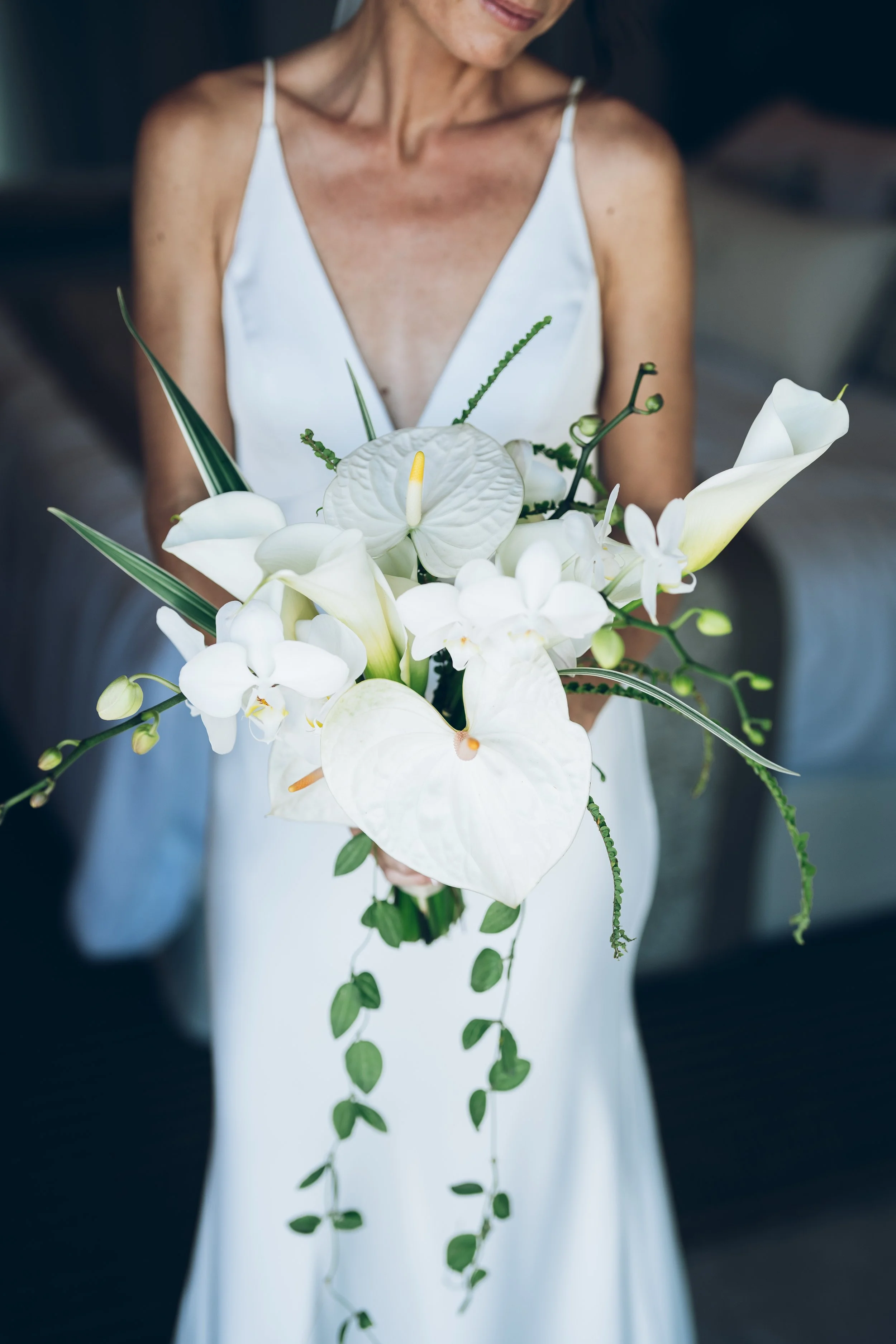 Une femme porte une robe blanche et tient un bouquet de fleurs blanches, principalement des calla lilies et des orchidées, en avant-plan.