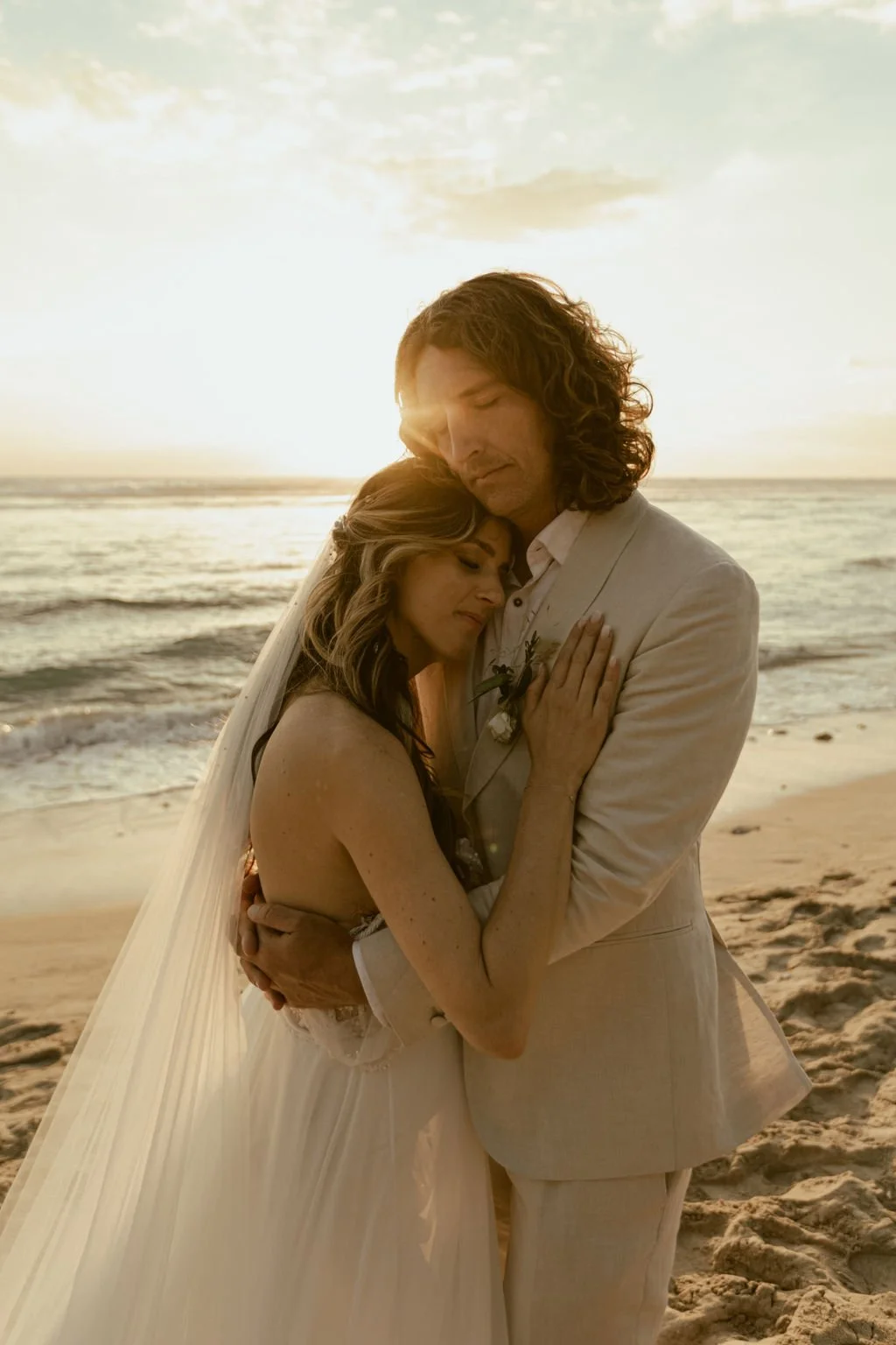 Un couple adorable en mariage sur la plage au coucher du soleil, se tenant étroitement dans un bisou tendre.