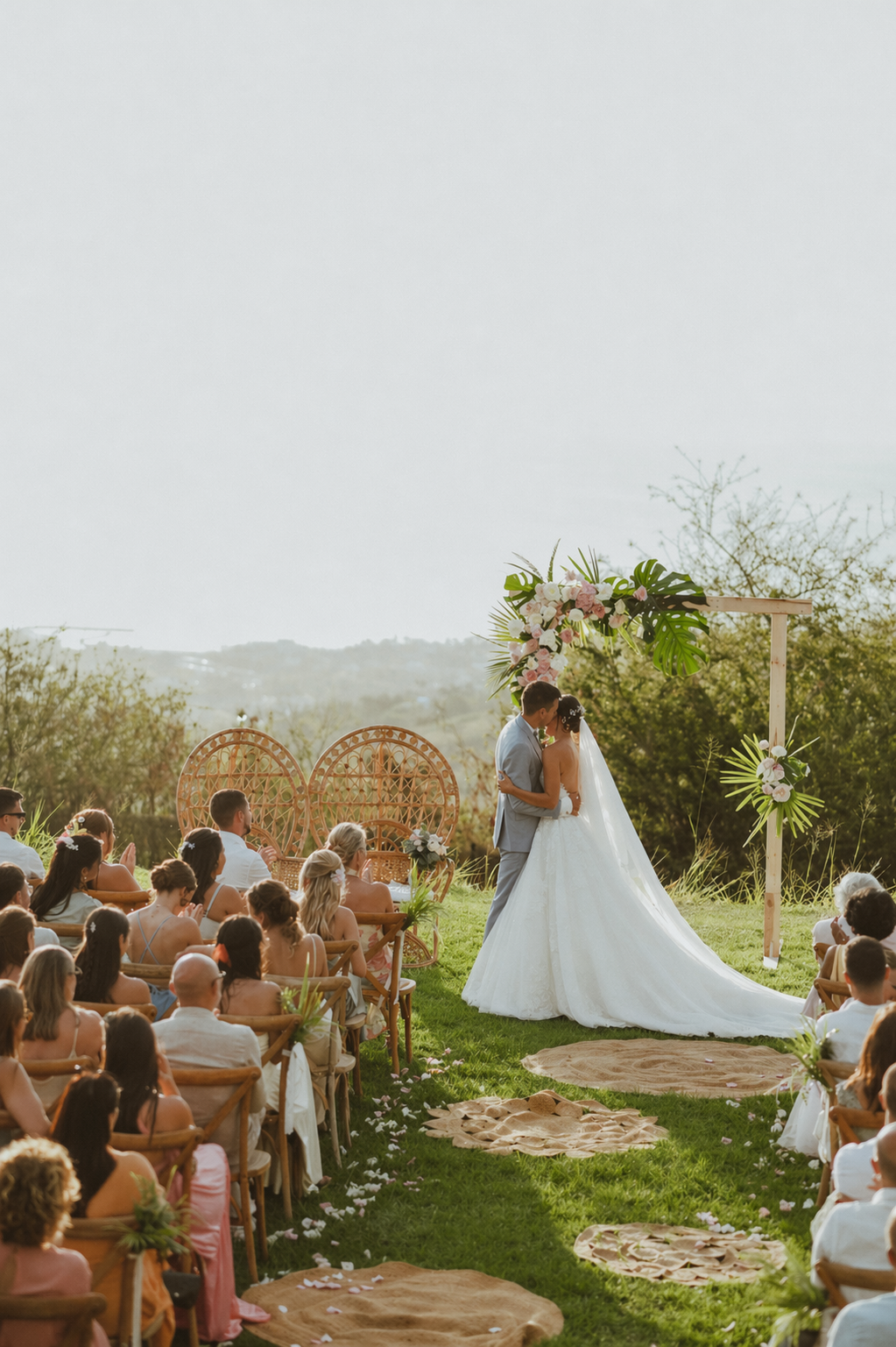 Un mariage en plein air avec deux personnes qui s'embrassent devant un arch en fleurs, entourées d'invités assis sur des chaises en bois