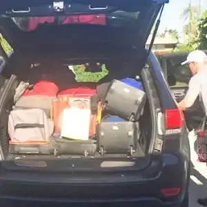 Open car trunk filled with luggage and bags, with a person standing nearby.