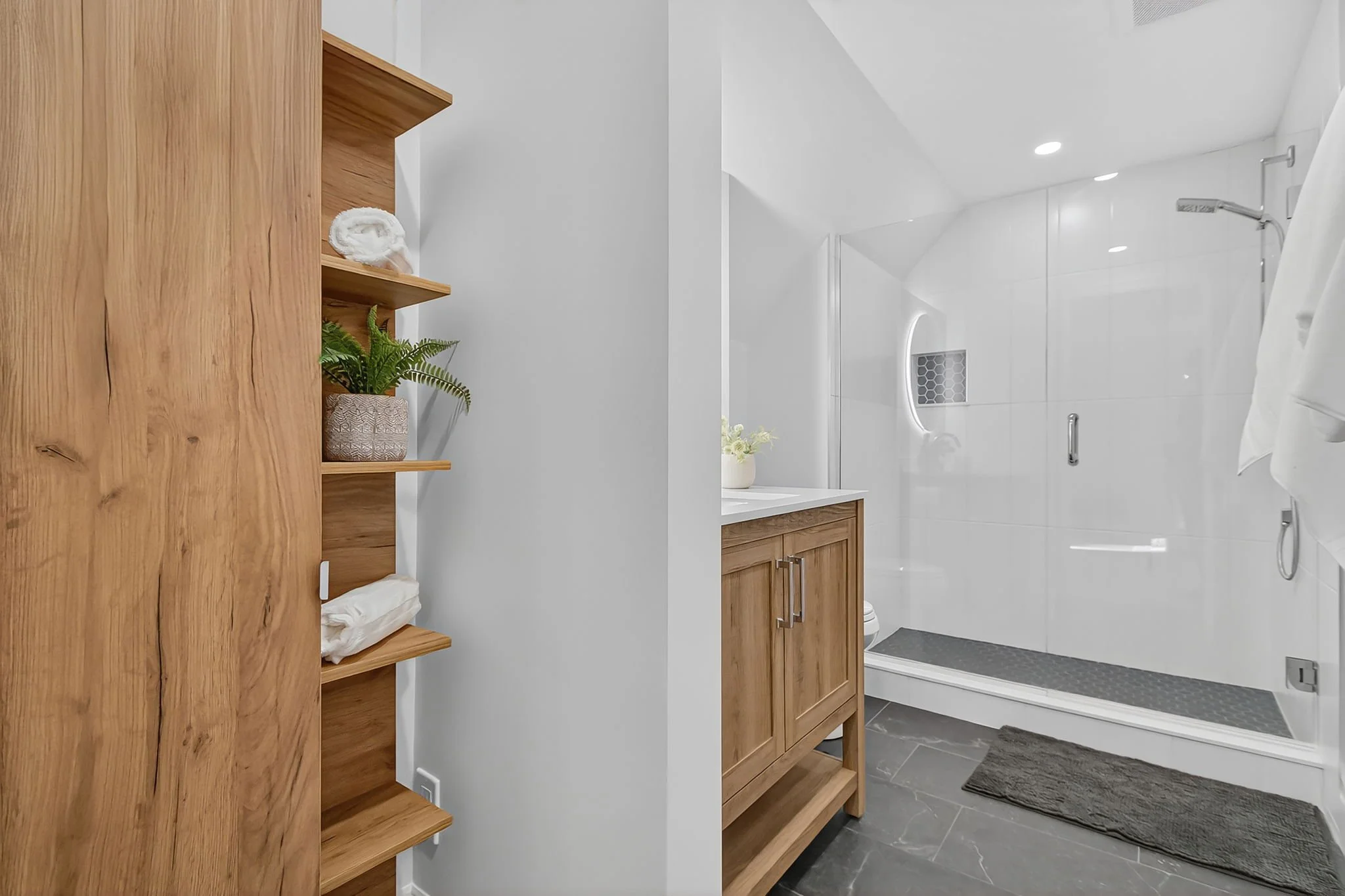 Bathroom with wooden cabinets, a shower with a glass door, gray floor tiles, and white walls.