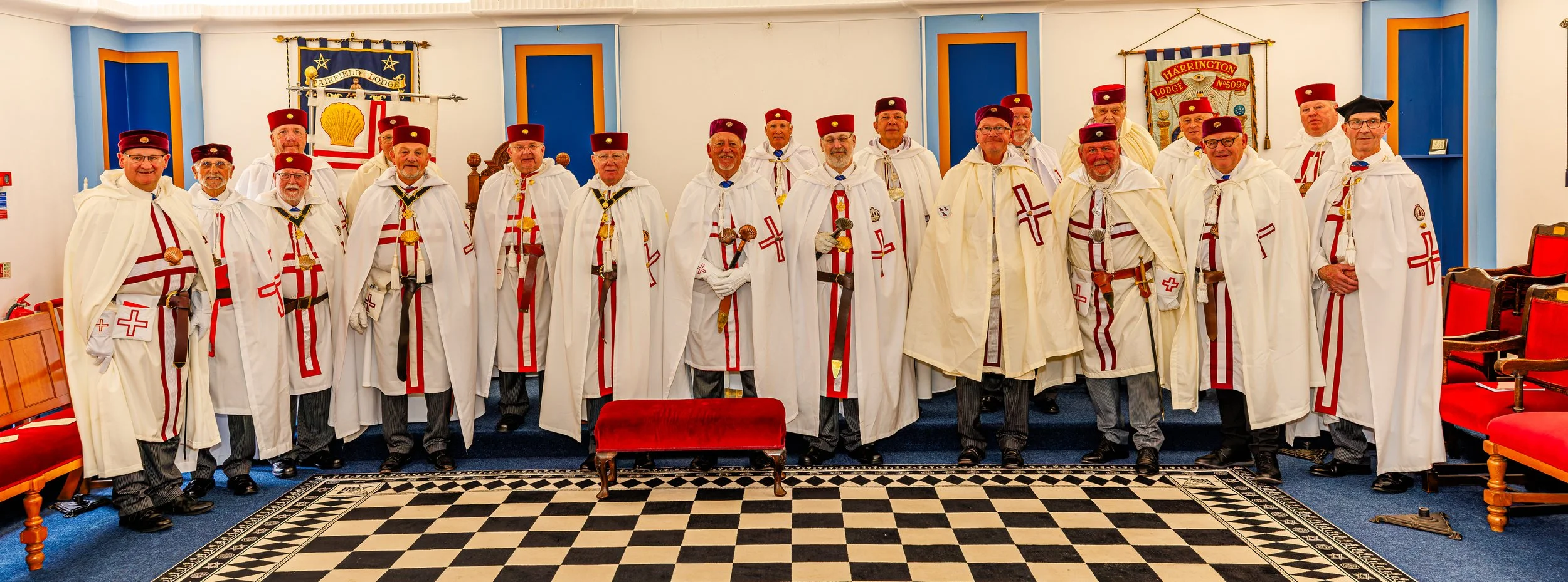 Group of men dressed in Scottish and Masonic regalia, standing indoors in a lodge room with blue and orange decorations, posing for a photo.
