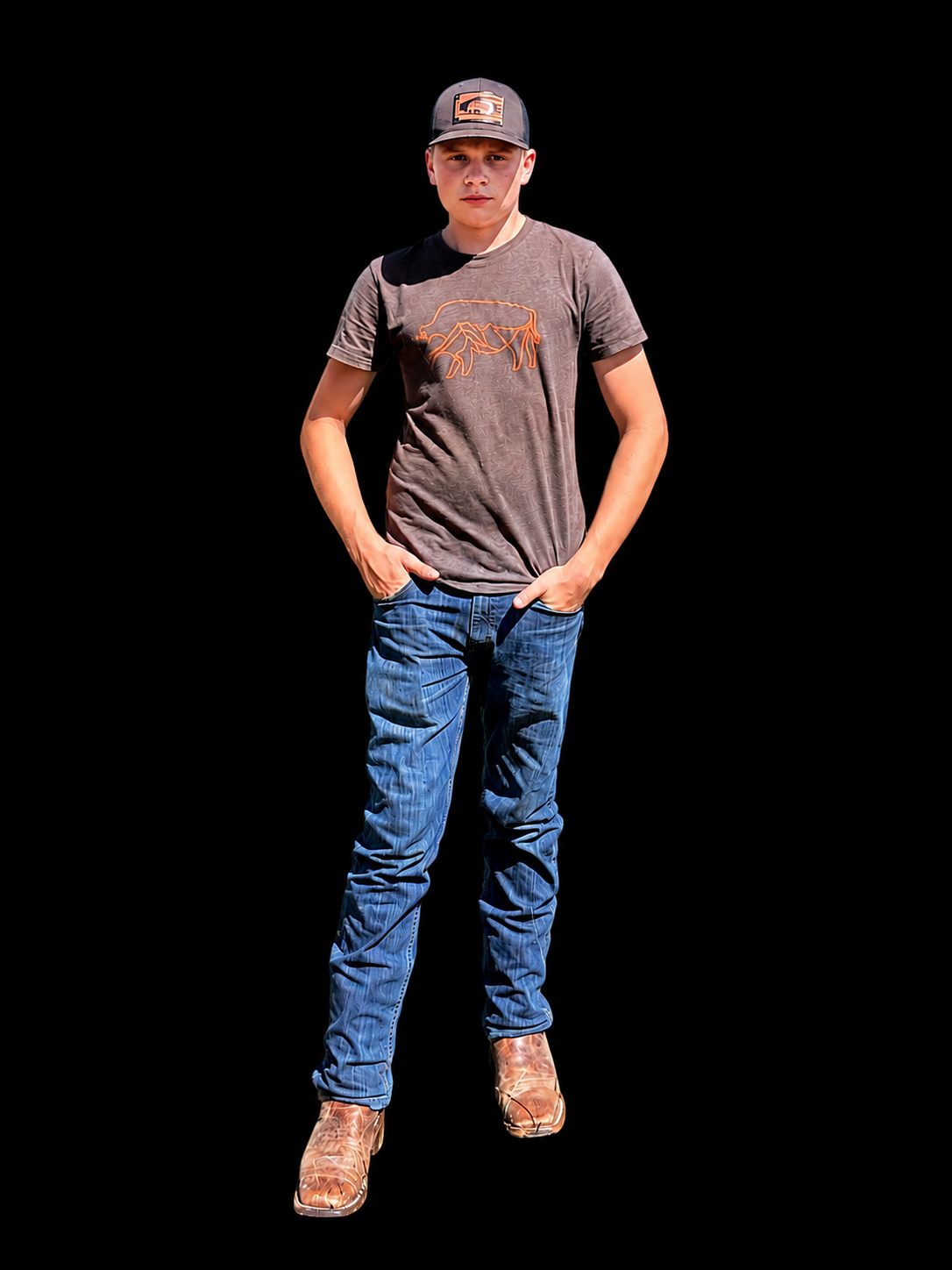 Young man standing with hands in pockets, wearing a cap, a t-shirt with a bull logo, jeans, and cowboy boots, against a black background.