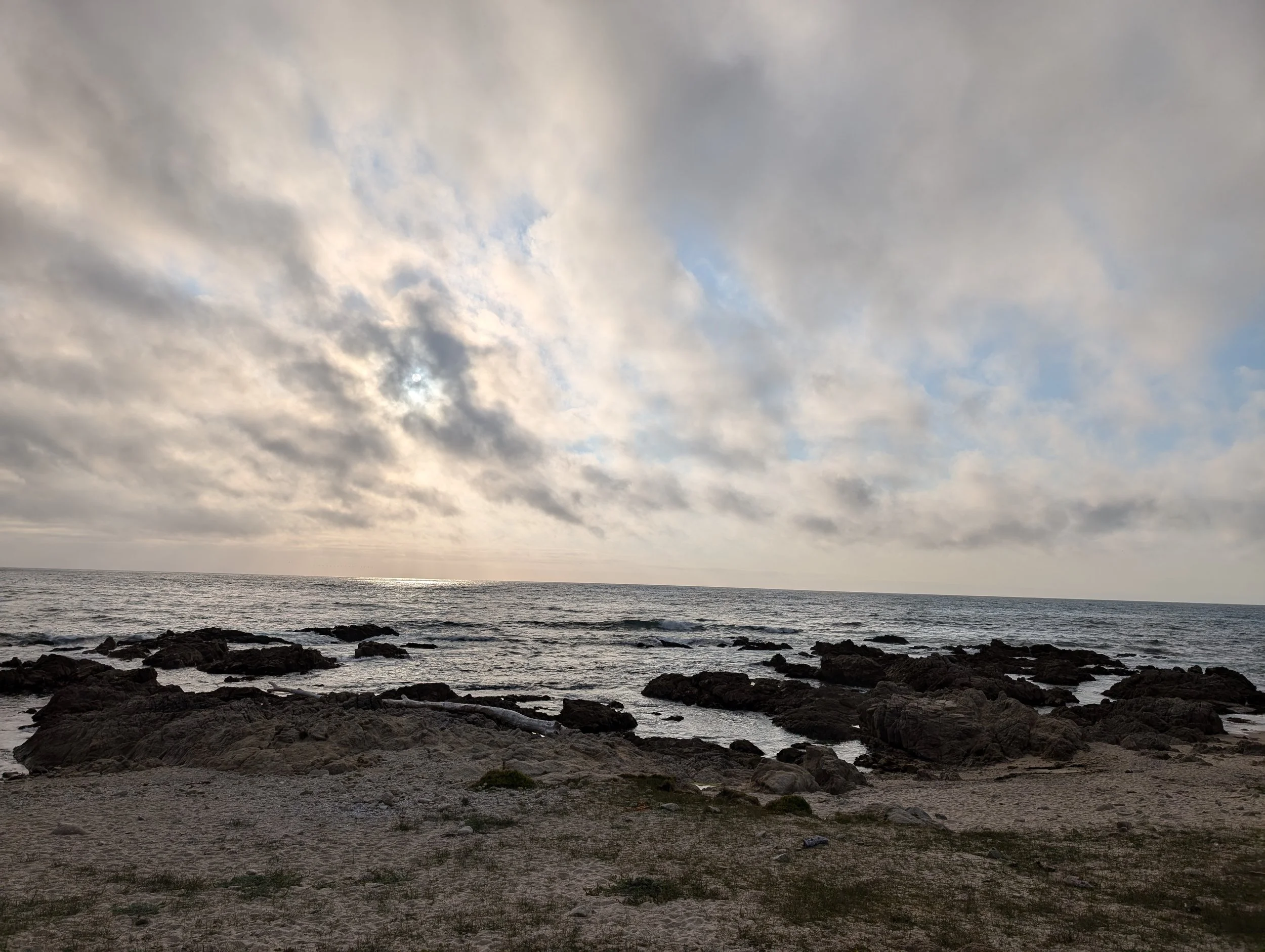 A cloudy sky over a rocky shoreline with some water visible in the distance under an overcast sky.