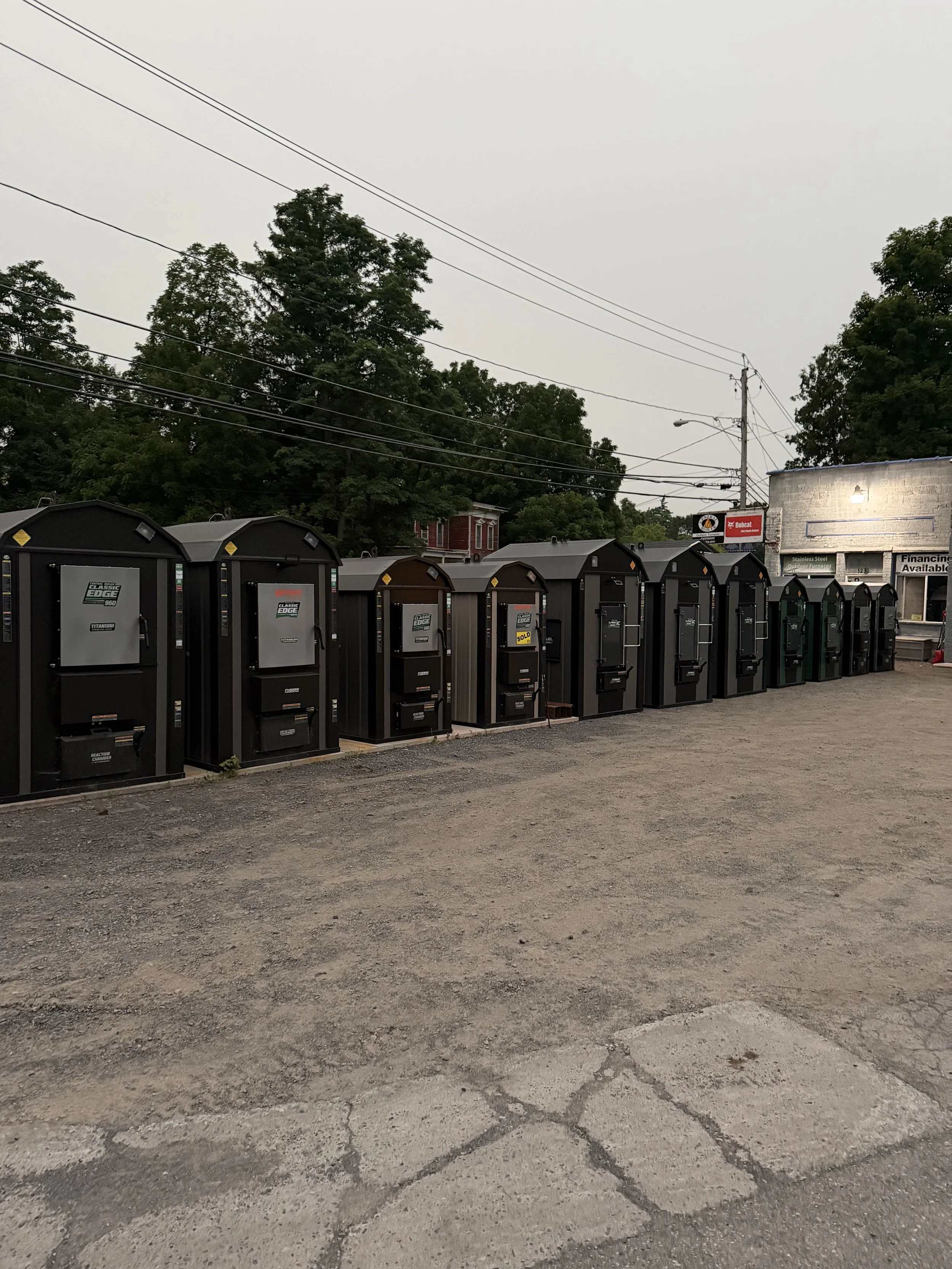 Row of black mailboxes outside a building with trees and power lines in the background.