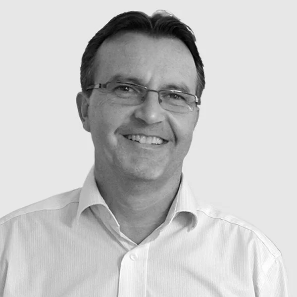Schwarz-weiße Porträtaufnahme eines lächelnden Mannes mit Brille, trägt ein weißes Hemd.