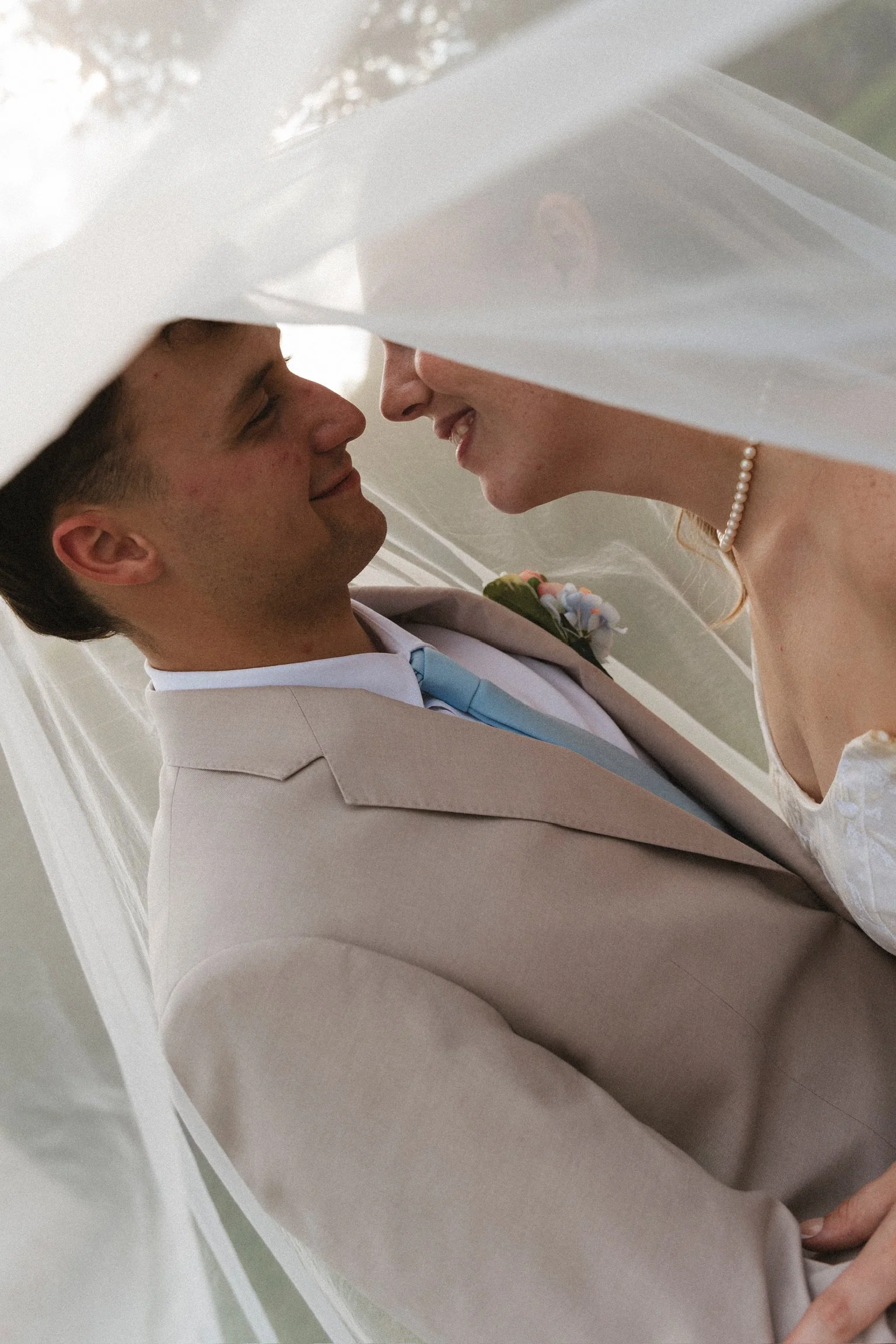 Happy bride and groom smiling and leaning close together under wedding veil during wedding ceremony.