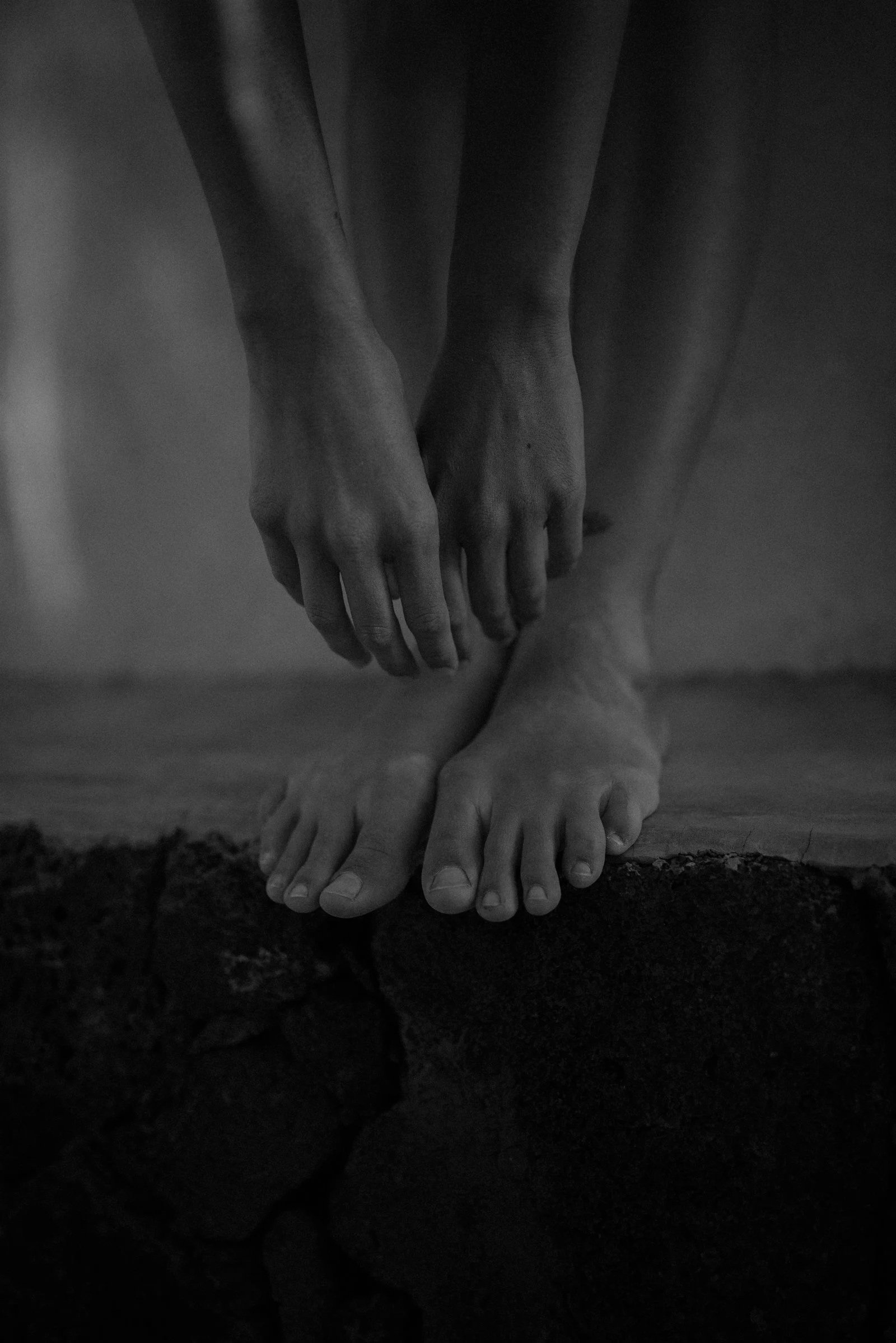 Black and white image of hands and feet resembling a human figure, with hands above and feet at the bottom, on a rocky surface.