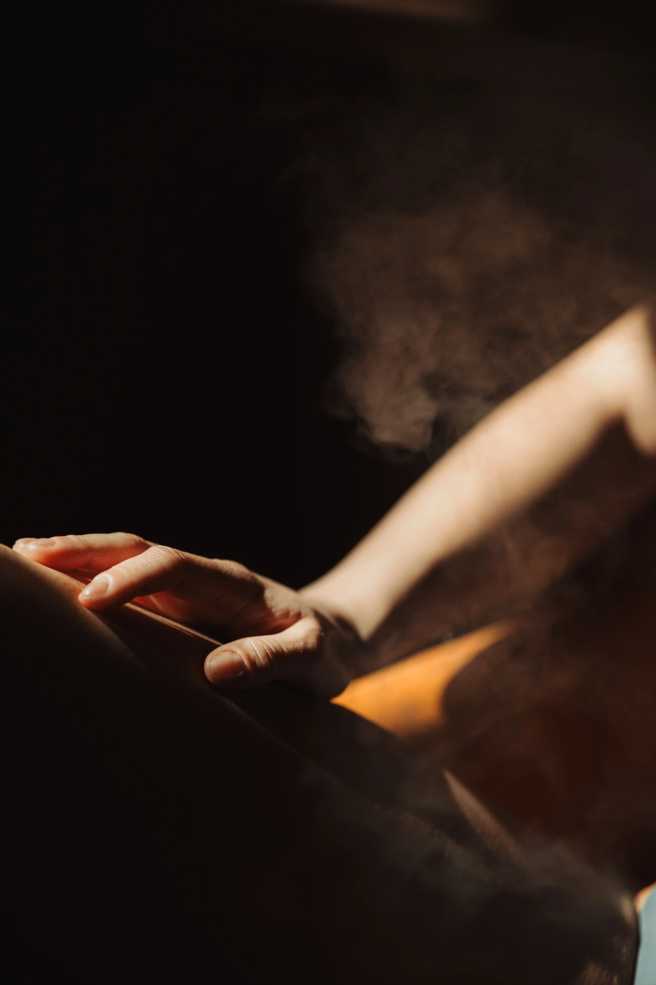 Close-up of a person's hand holding a smartphone, with the person wearing a light-colored shirt, only the hand and part of the arm are visible, in a dimly lit setting.