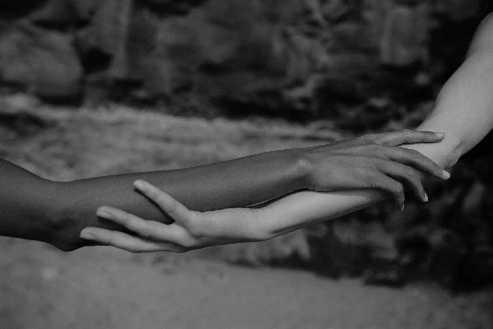 Two hands, one dark-skinned and one light-skinned, interlocked and touching.