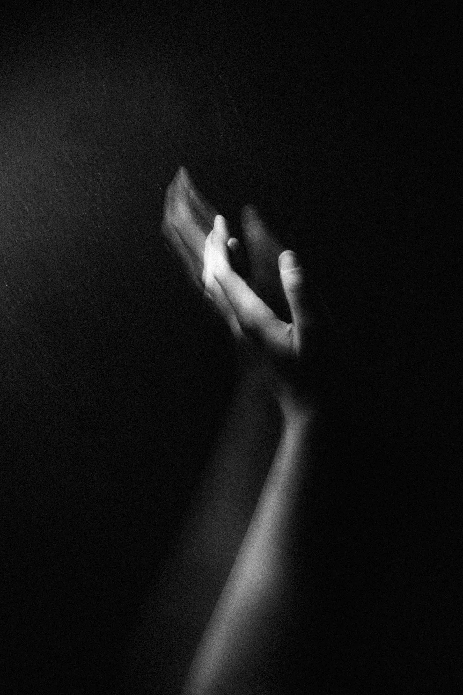 A black and white photo of a hand reaching out to touch a mirror
