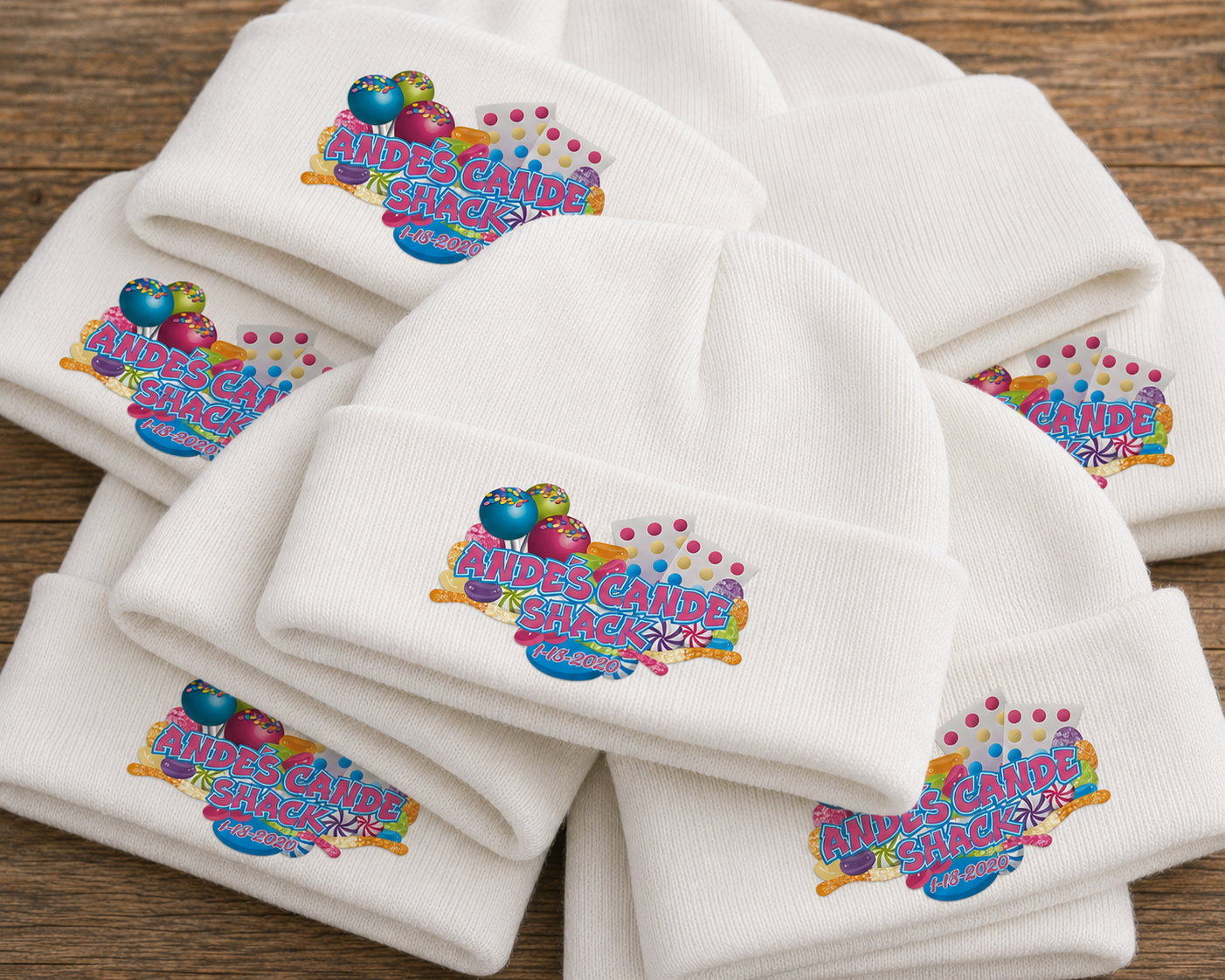 White knit beanies with colorful logo patches reading "Andes Cande Shack" and the date "1-18-2020," arranged on a wooden surface.