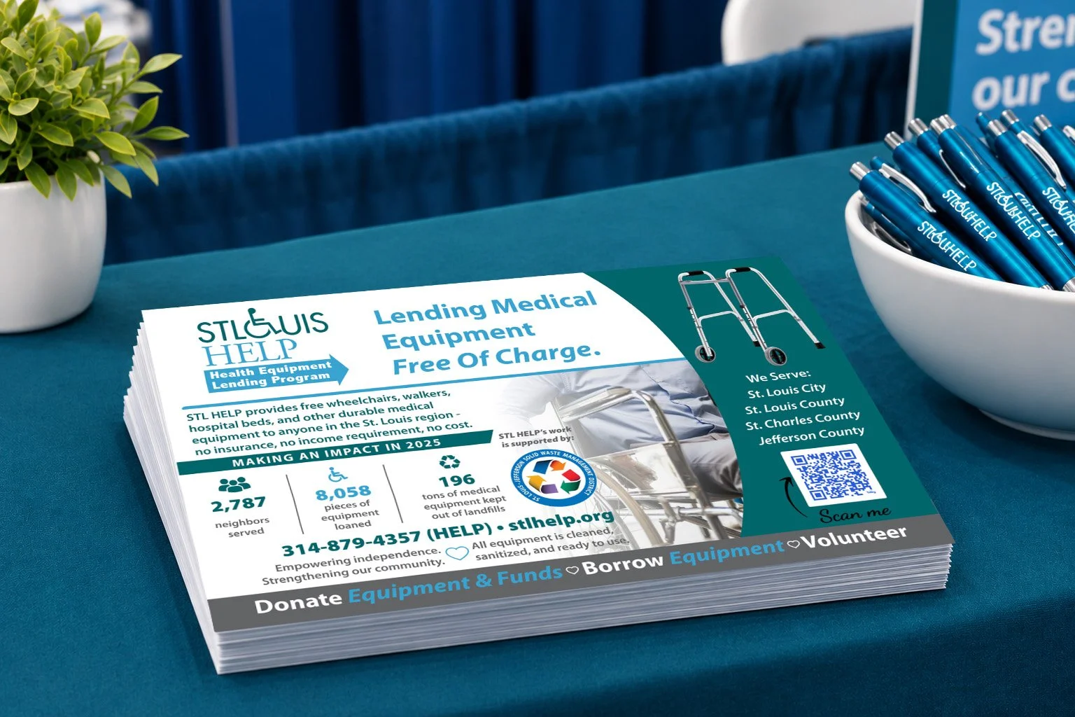 Flyer for STL HELP promoting free medical equipment lending program with text about services in St. Louis City, County, and Jefferson County, including contact and donation information, with pens and a potted plant nearby.