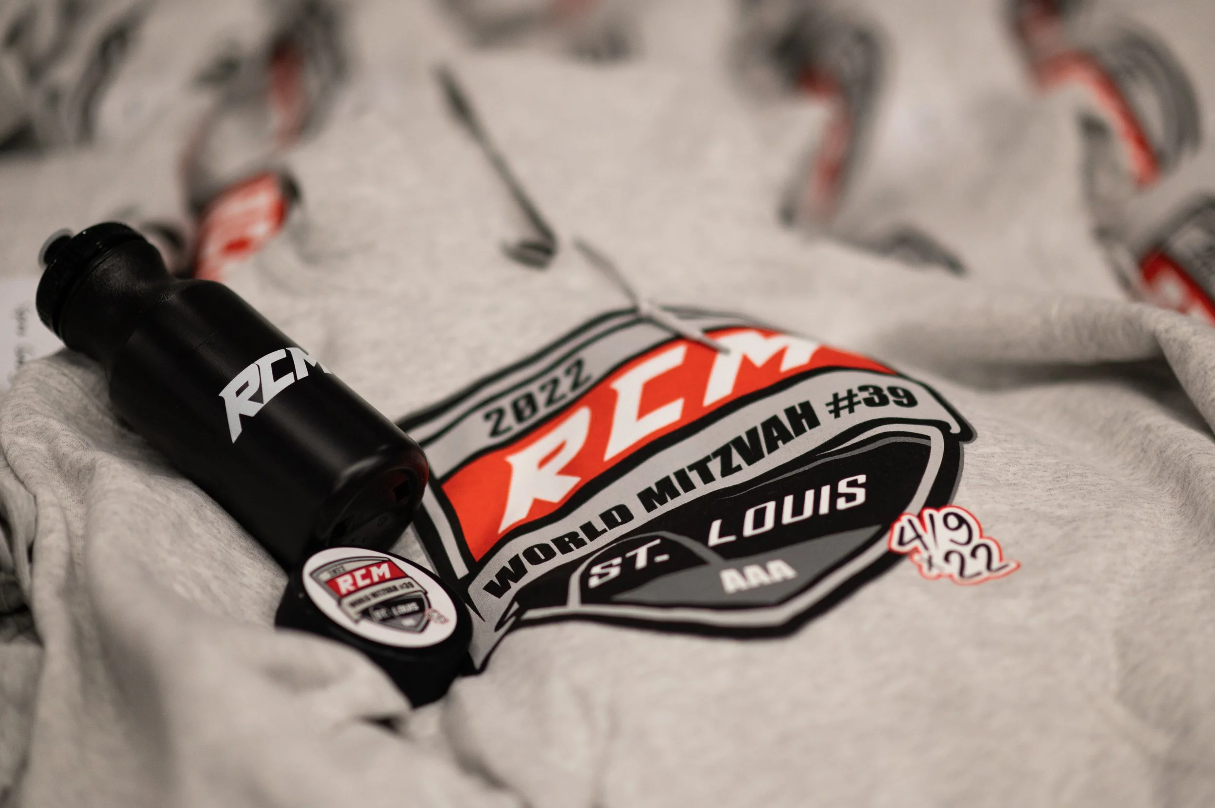 A black racing bicycle frame with REM branding lying on a white cloth with a circular logo for the 2022 St. Louis World Muay Thai Championship event, and part of a gray sweatshirt visible.
