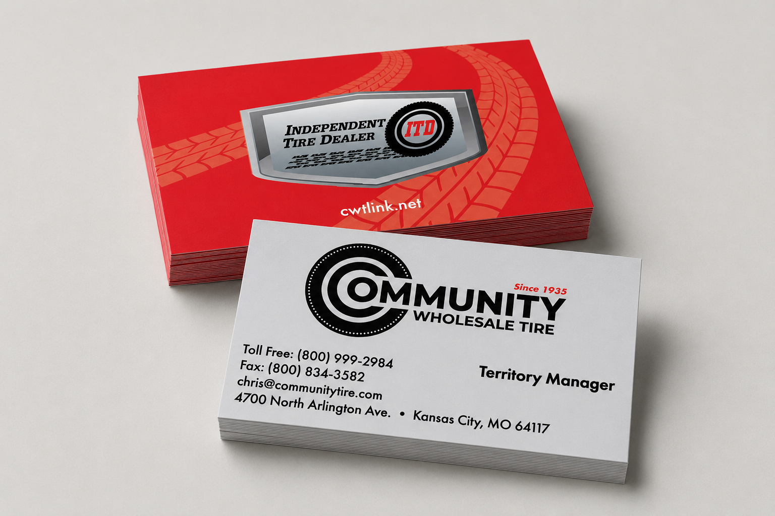 Business cards for Community Wholesale Tire and Independent Tire Dealer, featuring contact information and branding, placed on a white surface with a red tire track pattern on one card.