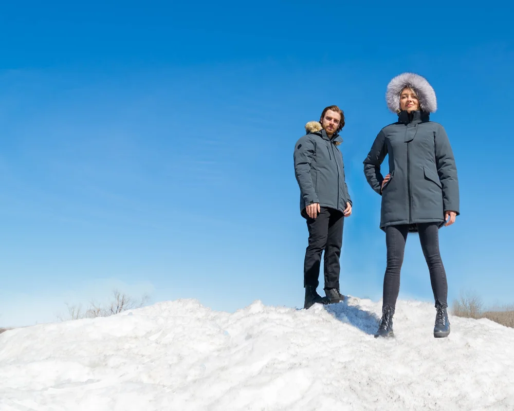 Two people wearing KLO winter parkas standing on a snowbank