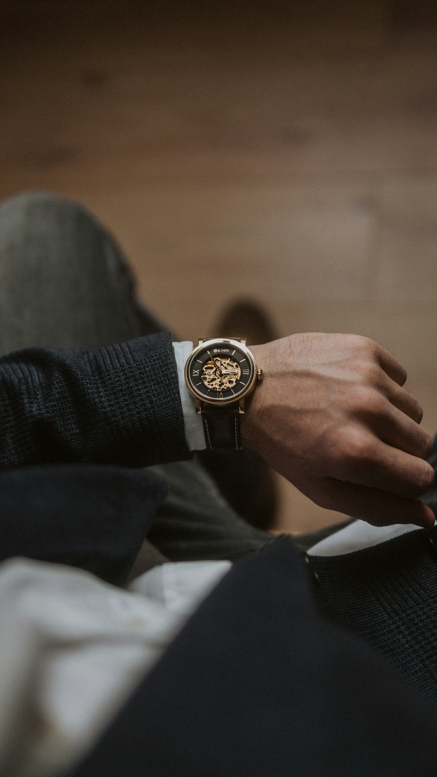 Close-up of a person's wrist wearing a black and gold skeleton wristwatch. The person is dressed in dark clothing, with the visible part of their hand and shirt cuff.