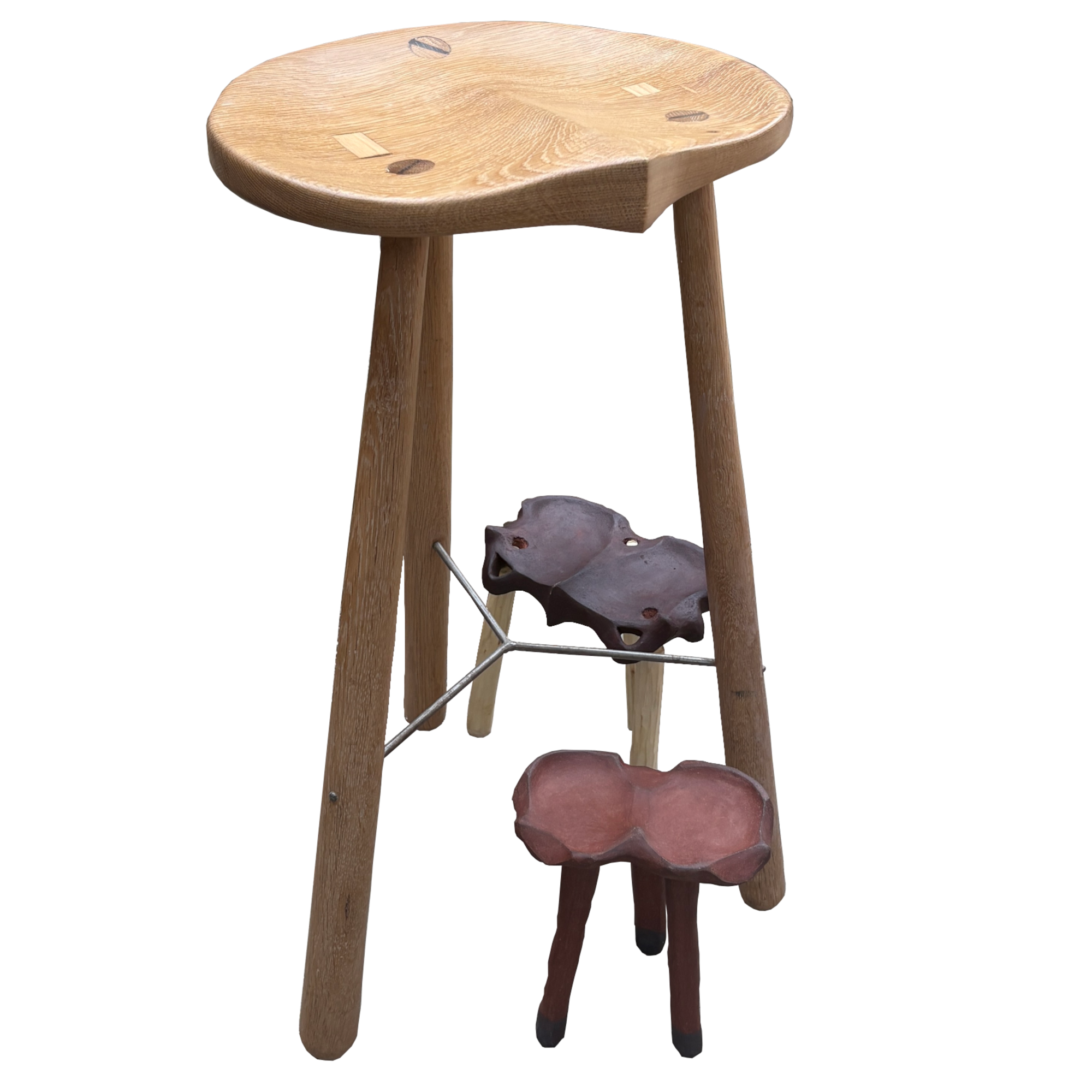 Wooden stool with three legs, a round seat, a rock resting on the ground near one of its legs.