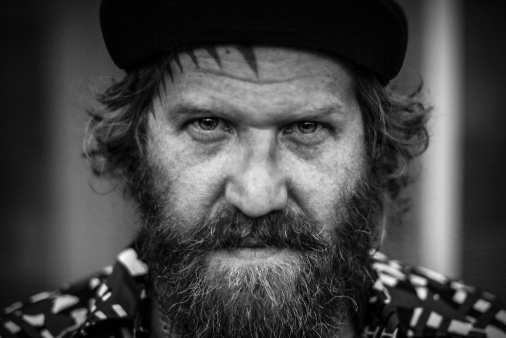 Black and white close-up of a man with a beard wearing a cap.