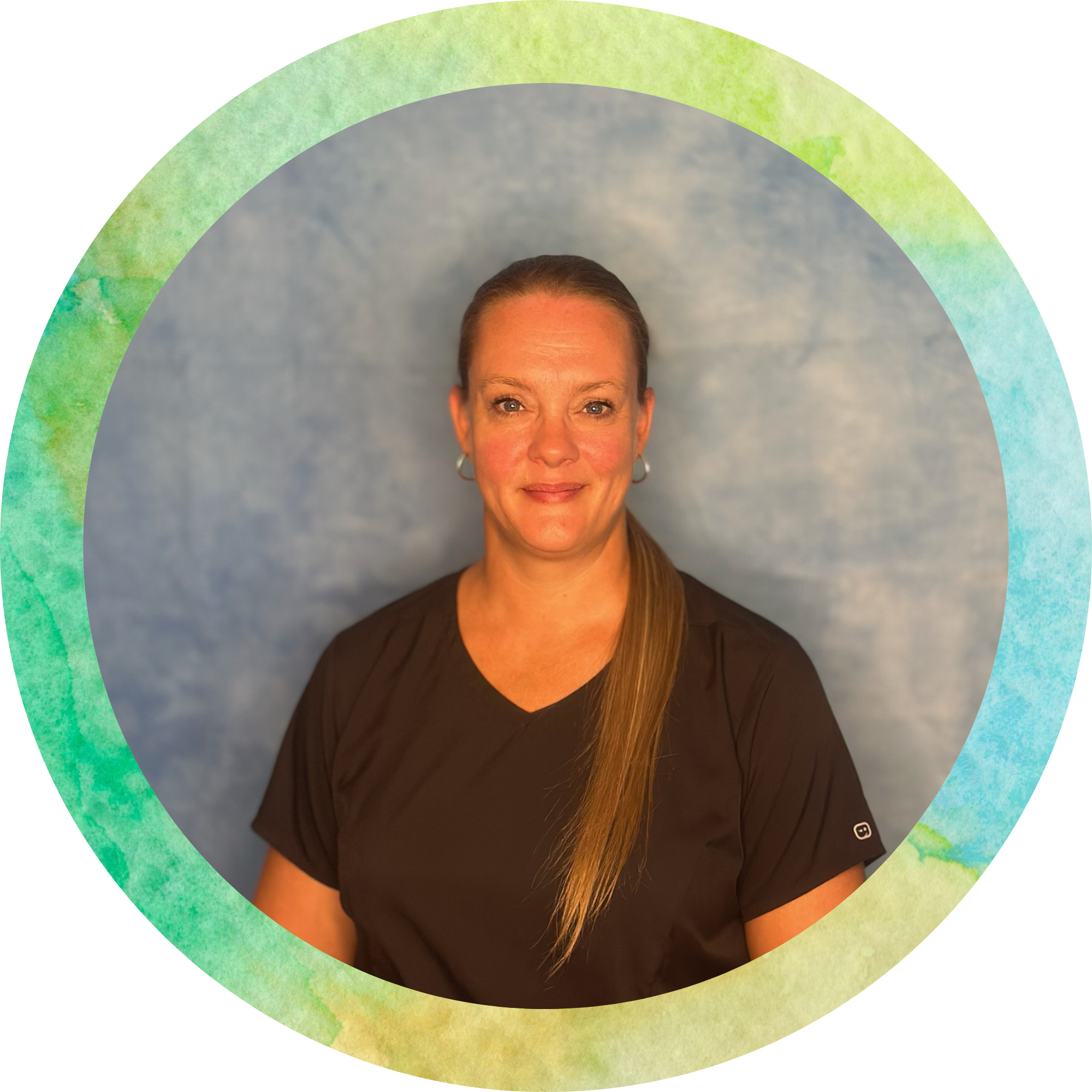 A woman with light skin, blue eyes, and long brown hair, wearing a black top, poses in front of a backdrop with watercolor textures and a rainbow-colored semi-circular overlay.