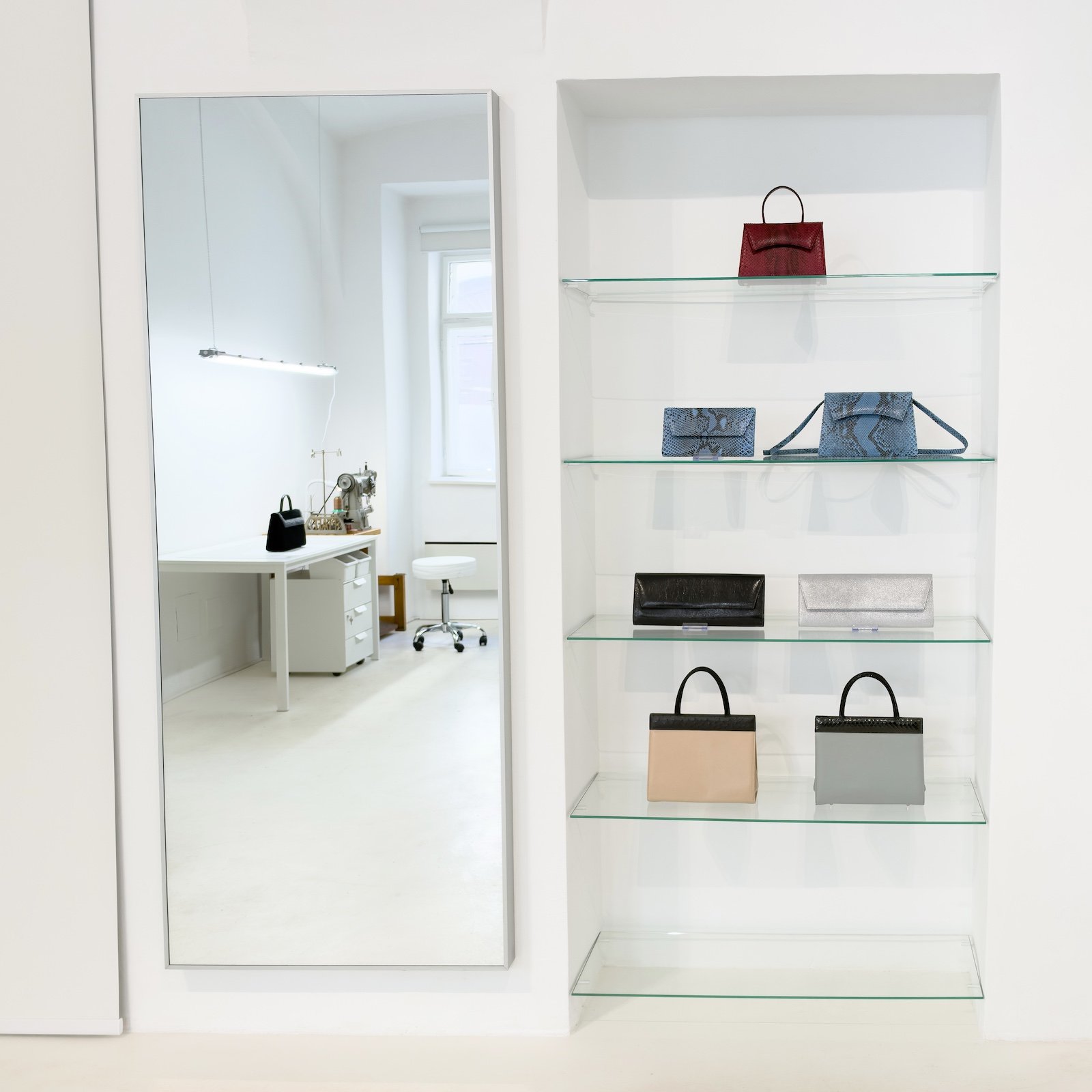 Verkaufsbereich der Werkstatt mit handgefertigten Taschen in einer beleuchteten Glasvitrine und einem großen Spiegel.