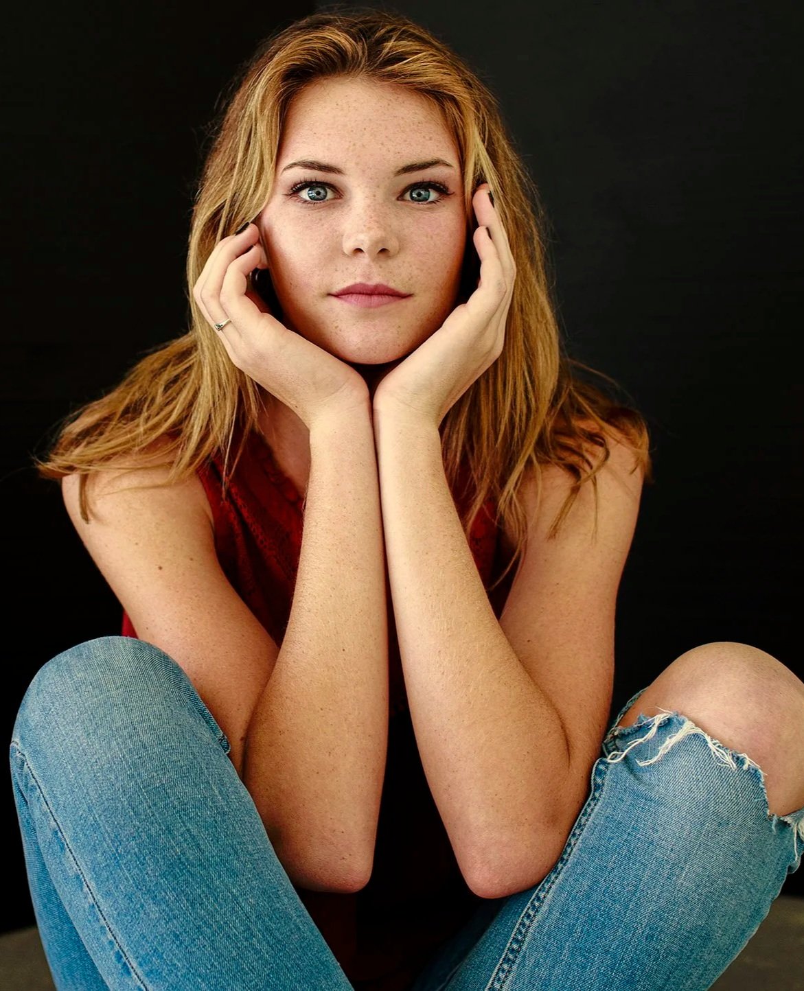 Close-up senior portrait with freckles, natural expression, and hands framing her face.