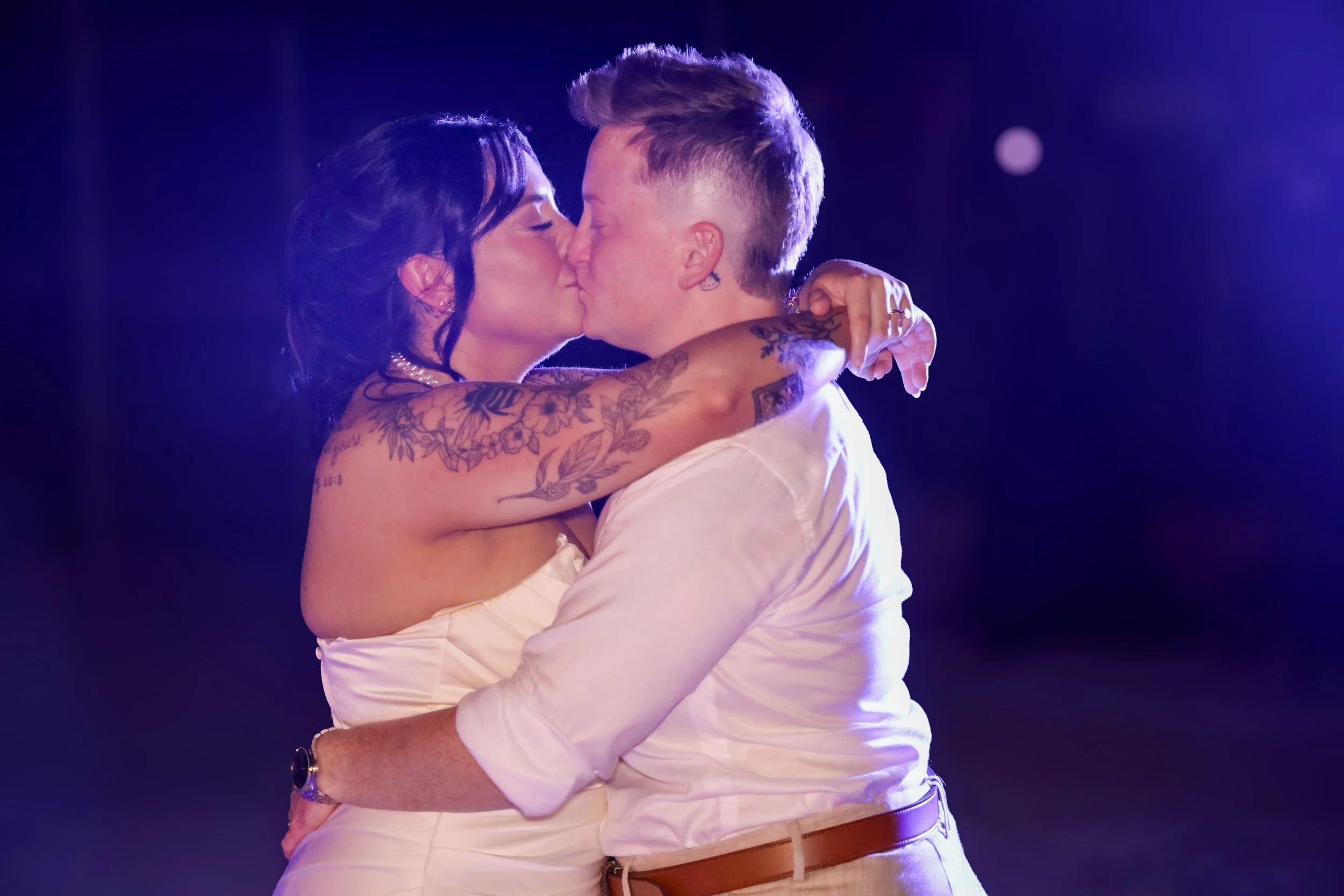 A couple kissing while embracing each other on a dance floor with purple lighting.