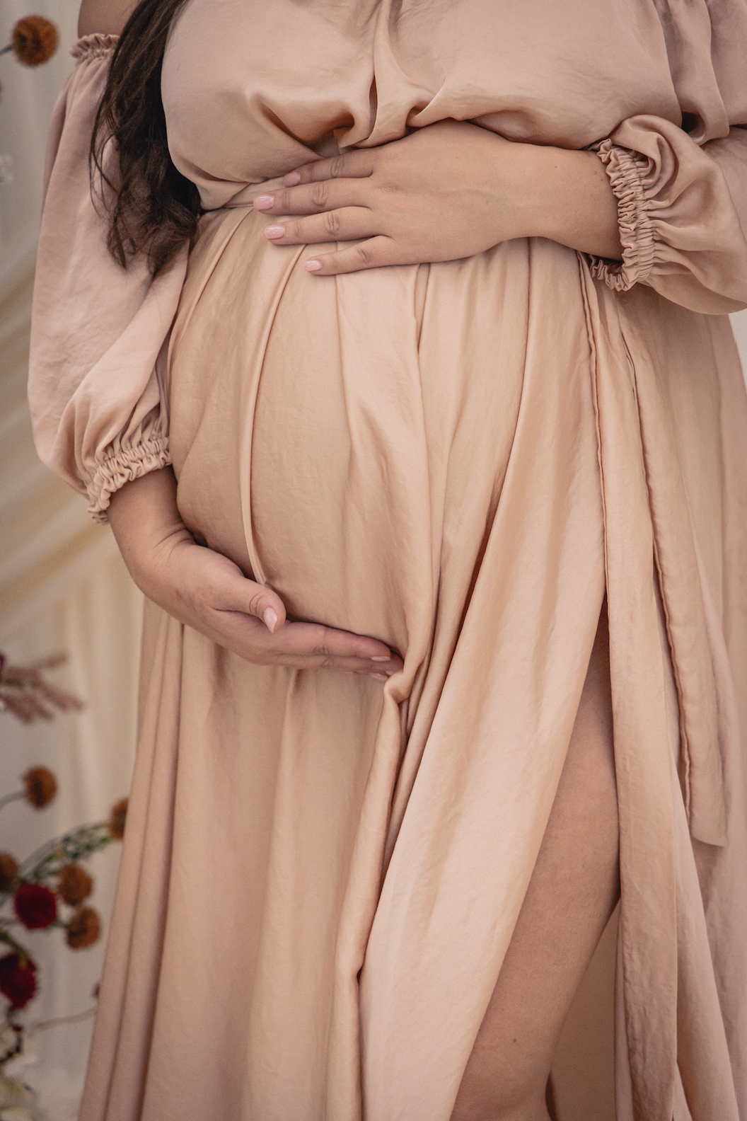 Close-up of a pregnant woman in a beige dress holding her belly with both hands.