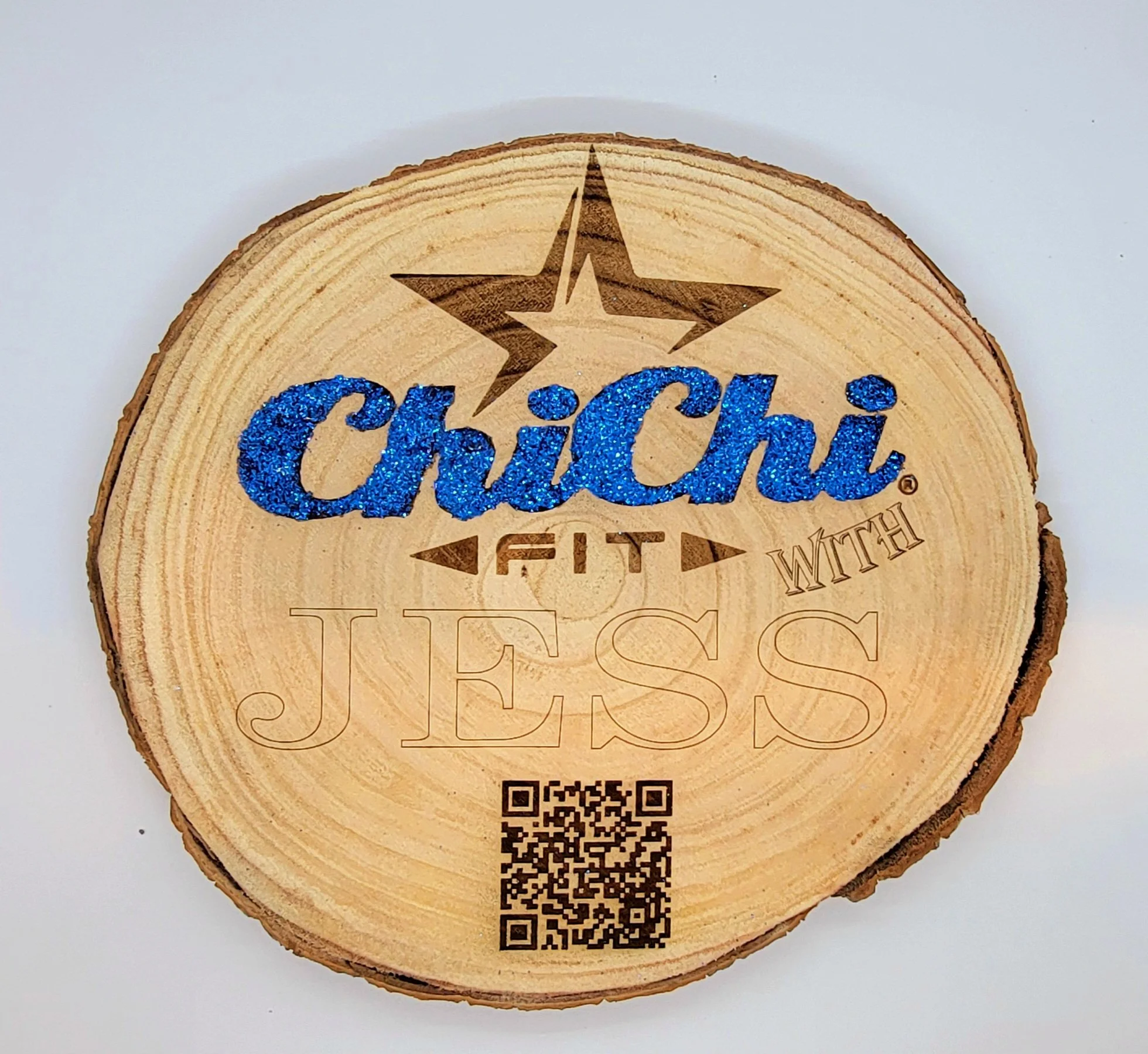 A round wooden slice with a star engraved at the top and the word "Chichi" in blue glitter and black text. There is a QR code at the bottom of the slice.