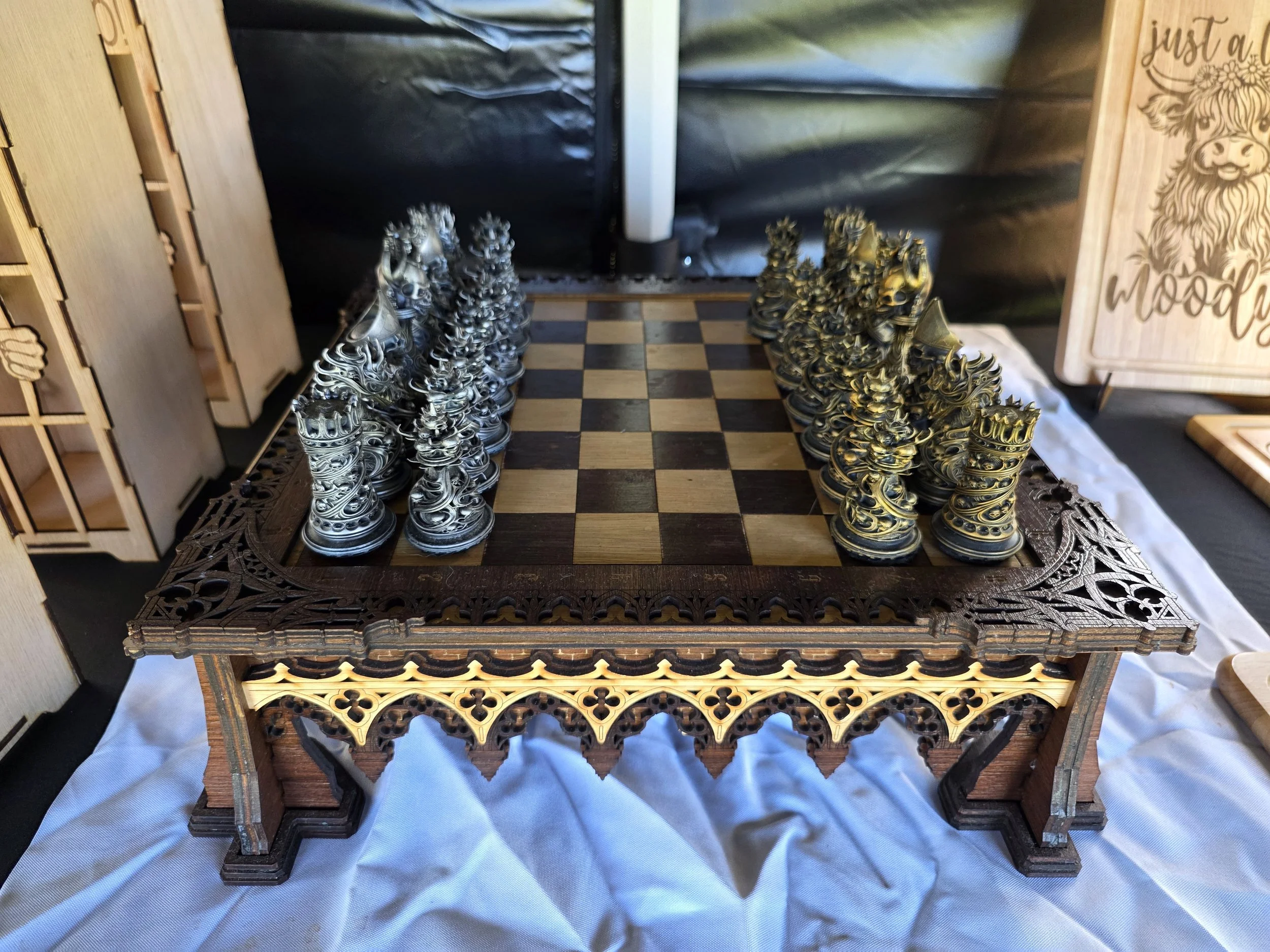 A chess set with intricately designed metallic pieces arranged on a decorative wooden chessboard.