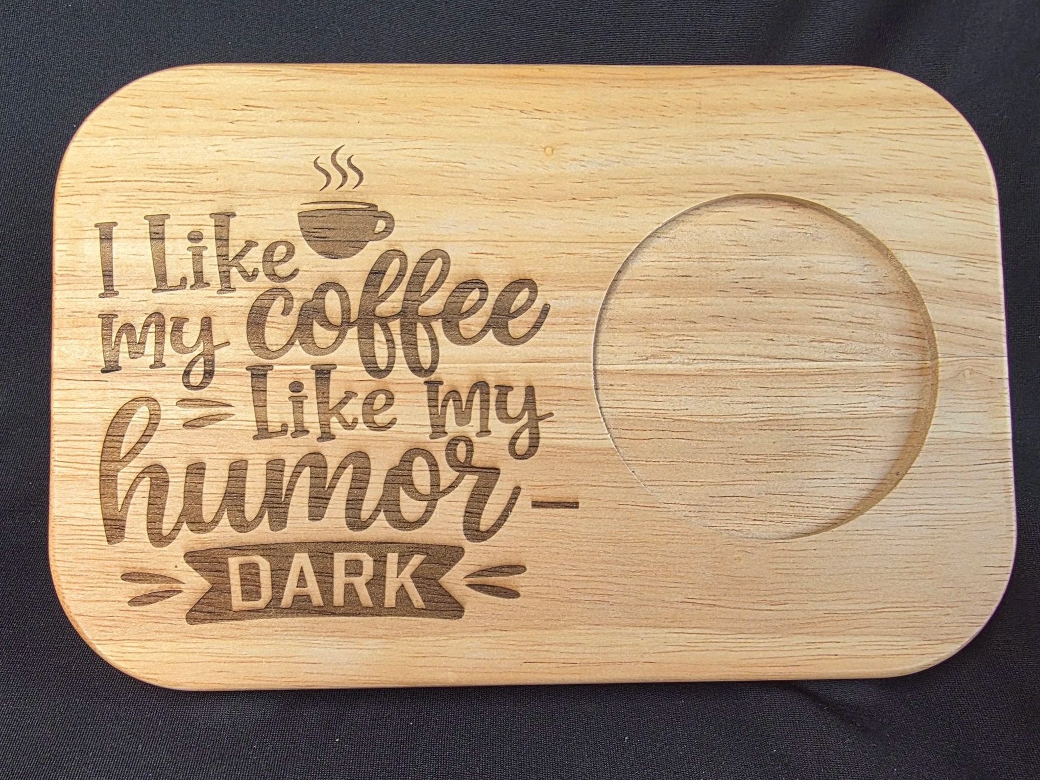 Wooden tray with etched phrase 'I like my coffee black, like my... dark' and a circular indentation for a cup.